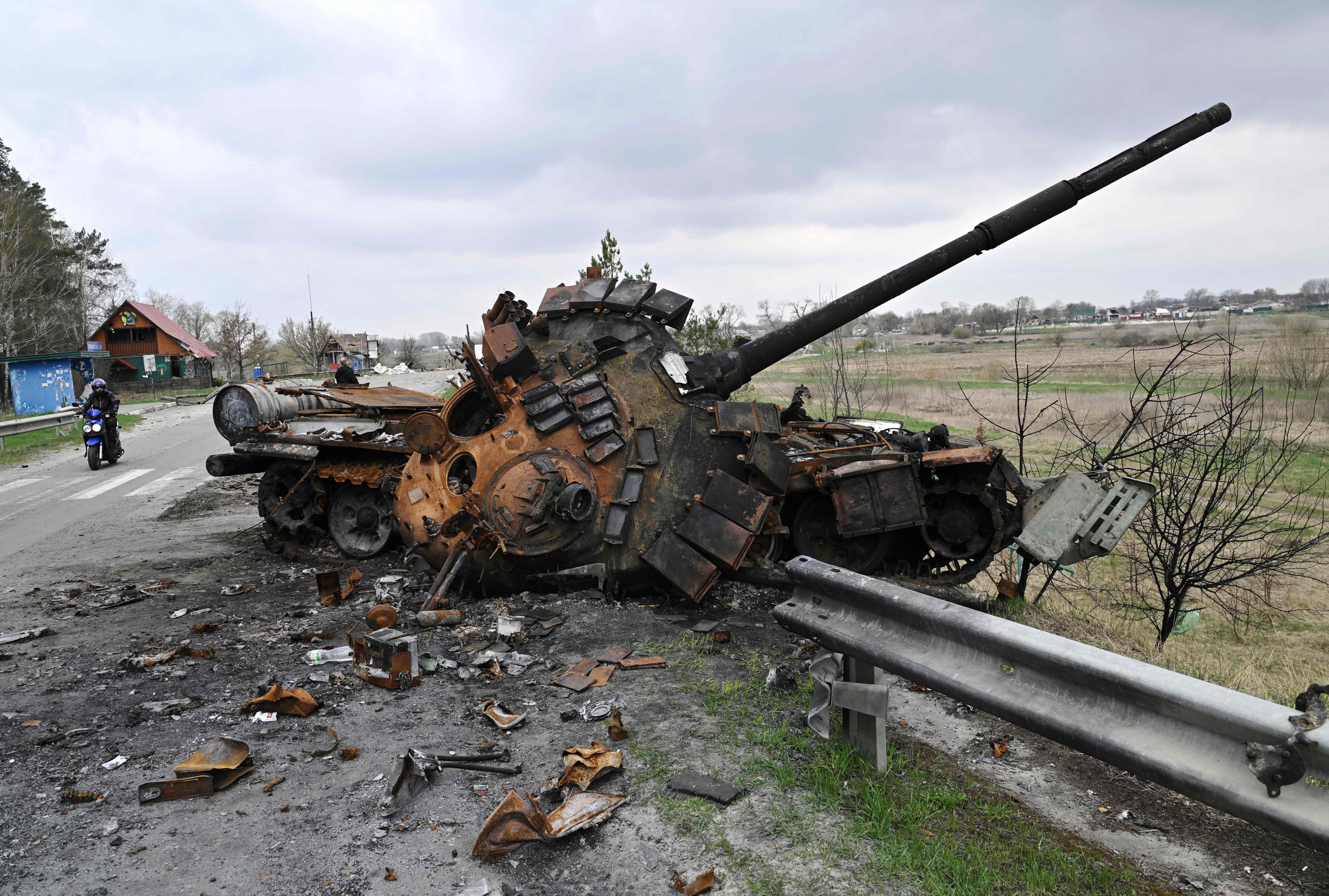A man ride a motorbike past a destroyed Russian tank on a road in the village of Rusaniv, in the Kyiv region on April 16, 2022. - Many of the nearly five million people who have fled Ukraine will not have homes to return to, the United Nations said on April 16, 2022, as another 40,000 fled the country in 24 hours. (Photo by Genya SAVILOV / AFP) (Photo by GENYA SAVILOV/AFP via Getty Images)
