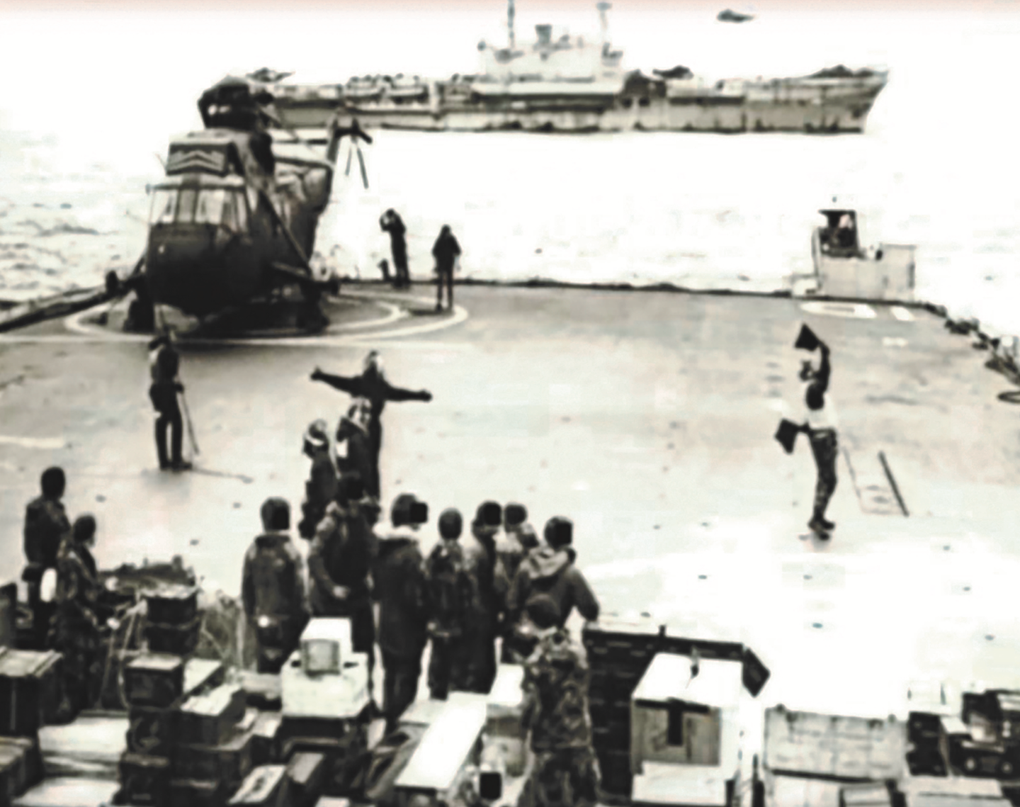 The flight deck of HMS <em>Intrepid</em> during the cross-decking operation from <em>Hermes</em> (shown in the background) on May 19. Some of the squadron’s stores are piled up in the foreground with some of the soldiers who had already made the trip over. This picture was taken during daylight, an hour or so before tragedy struck. <em>via publisher</em>