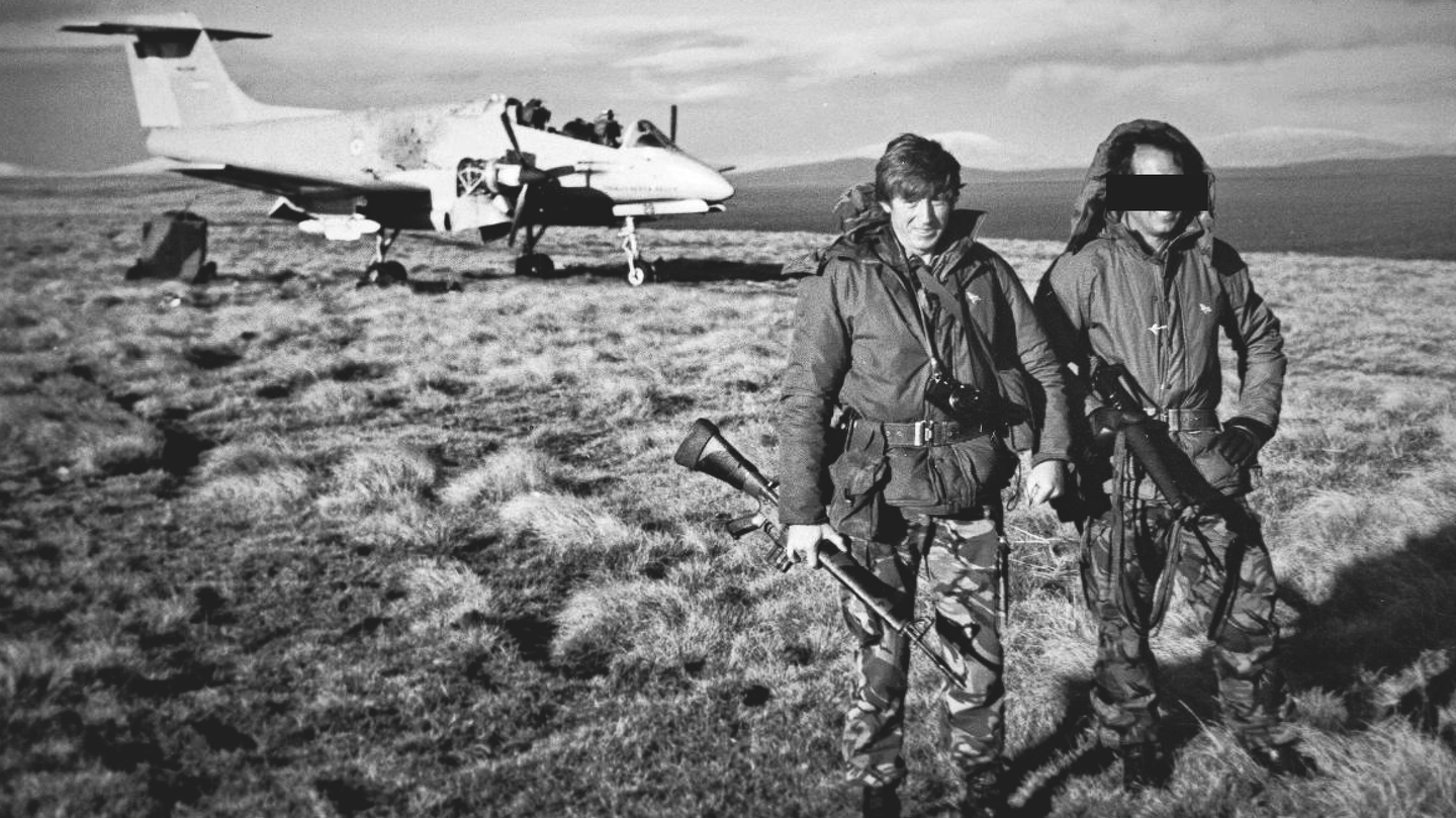 Maj. Cedric Delves, the officer commanding D Squadron, standing with the regiment’s operations officer by a destroyed Pucara on the airstrip at Pebble Island at the end of the war. <em>Antony Bysouth</em>