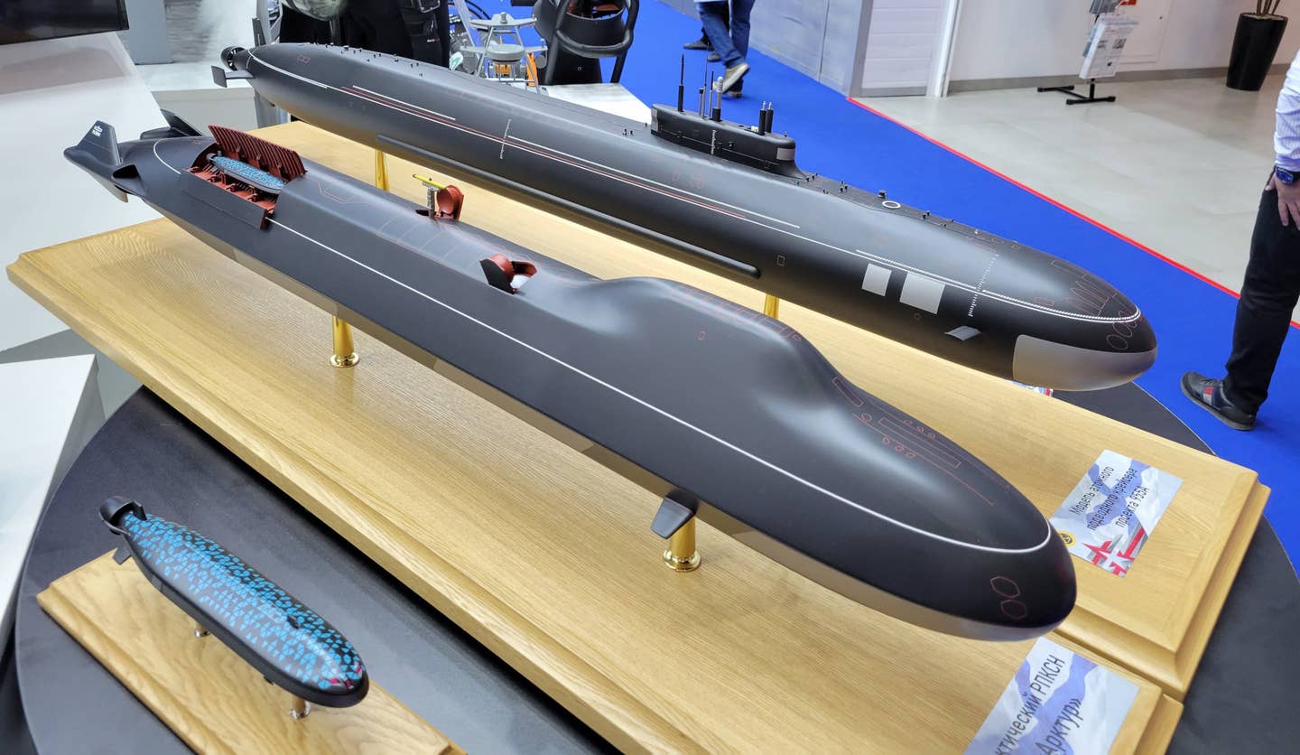 The models of the Arktur and Surrogate-V design concepts at Army 2022, in front, with a model of a Project 955A <em>Borei-A</em> class ballistic missile submarine behind them. <em>@MuxelAero</em>