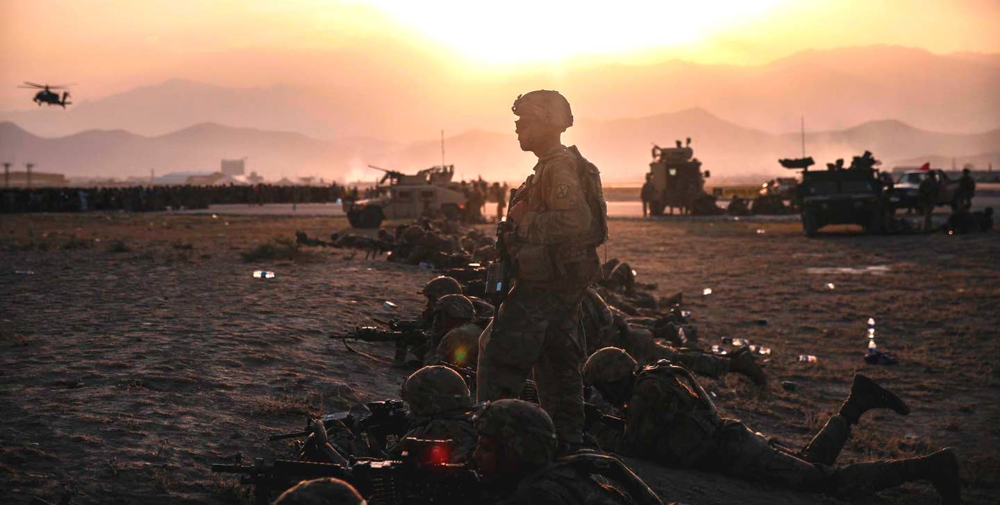 Members of the US Army's 10th Mountain Division, along with other US and local forces, maintain a hasty perimeter at Hamid Karzai International Airport on August 15, 2021. Throngs of Afghans and others hoping to flee by air can be seen to the left. <em>U.S. Marine Corps / Sgt. Isaiah Campbell</em>