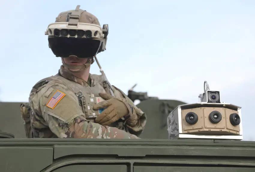 A US Army soldier wearing a prototype Integrated Visual Augmentation System (IVAS) stands in a Stryker wheeled armored vehicle during a test in 2021. A camera array associated with a distributed aperture system able to feed into the IVAS headset is also seen fitted to the vehicle. <em>US Army</em>