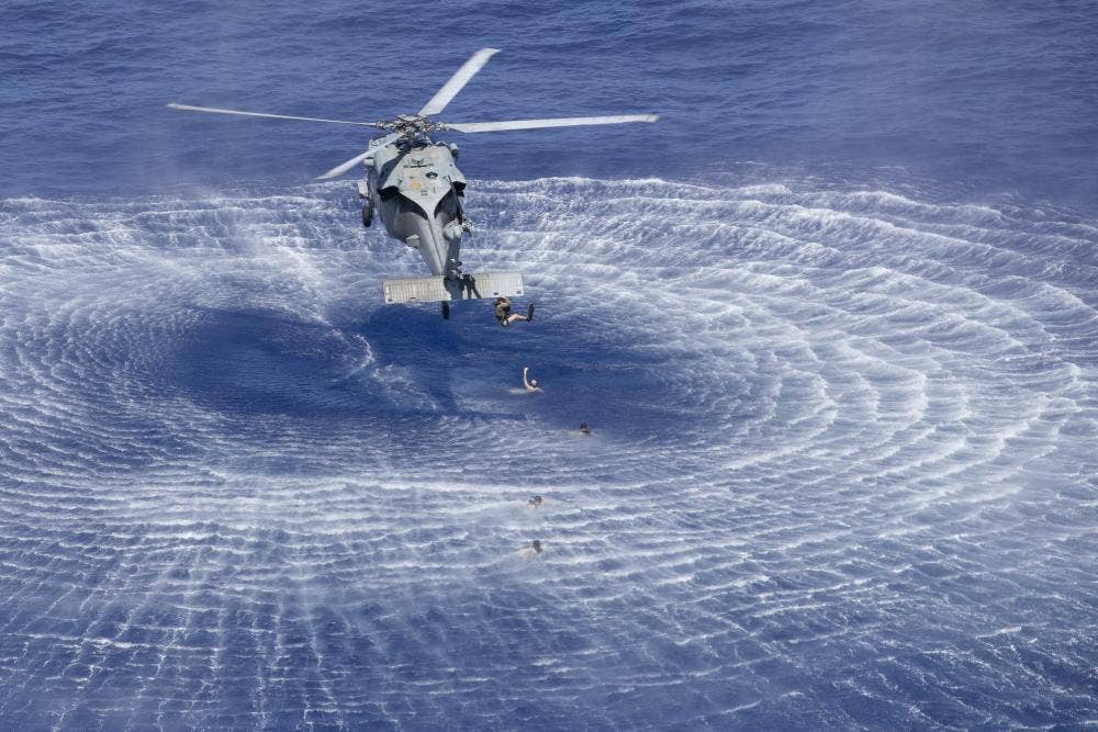 A naval air crewman jumps out of an MH-60S during search and rescue (SAR) swimmer training. <em>U.S. Navy</em>