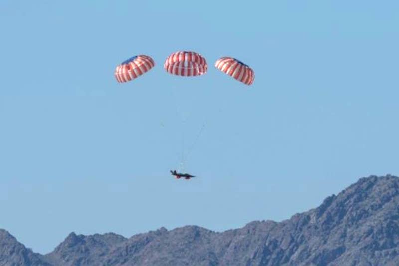 An XQ-58A descending under its parachutes after a mission. Also visible are inflatable airbags underneath to further cushion it when it hits the ground. <em>Kratos</em>