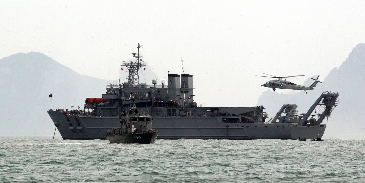The auxiliary submarine rescue ship <em>Cheonghaejin</em> works with a UH-60 helicopter during search and rescue operations at the site of the sinking of the ferry MV <em>Sewol</em> in April 2014. <em>Republic of Korea Armed Forces</em>