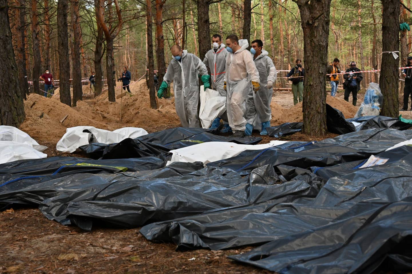 Forensics carry body bags in a forest near Izyum, eastern Ukraine, on September 19, 2022, where Ukrainian investigators have uncovered more than 440 graves after the city was recaptured from the Russians, bringing fresh claims of Russian atrocities. (Photo by SERGEY BOBOK/AFP via Getty Images)