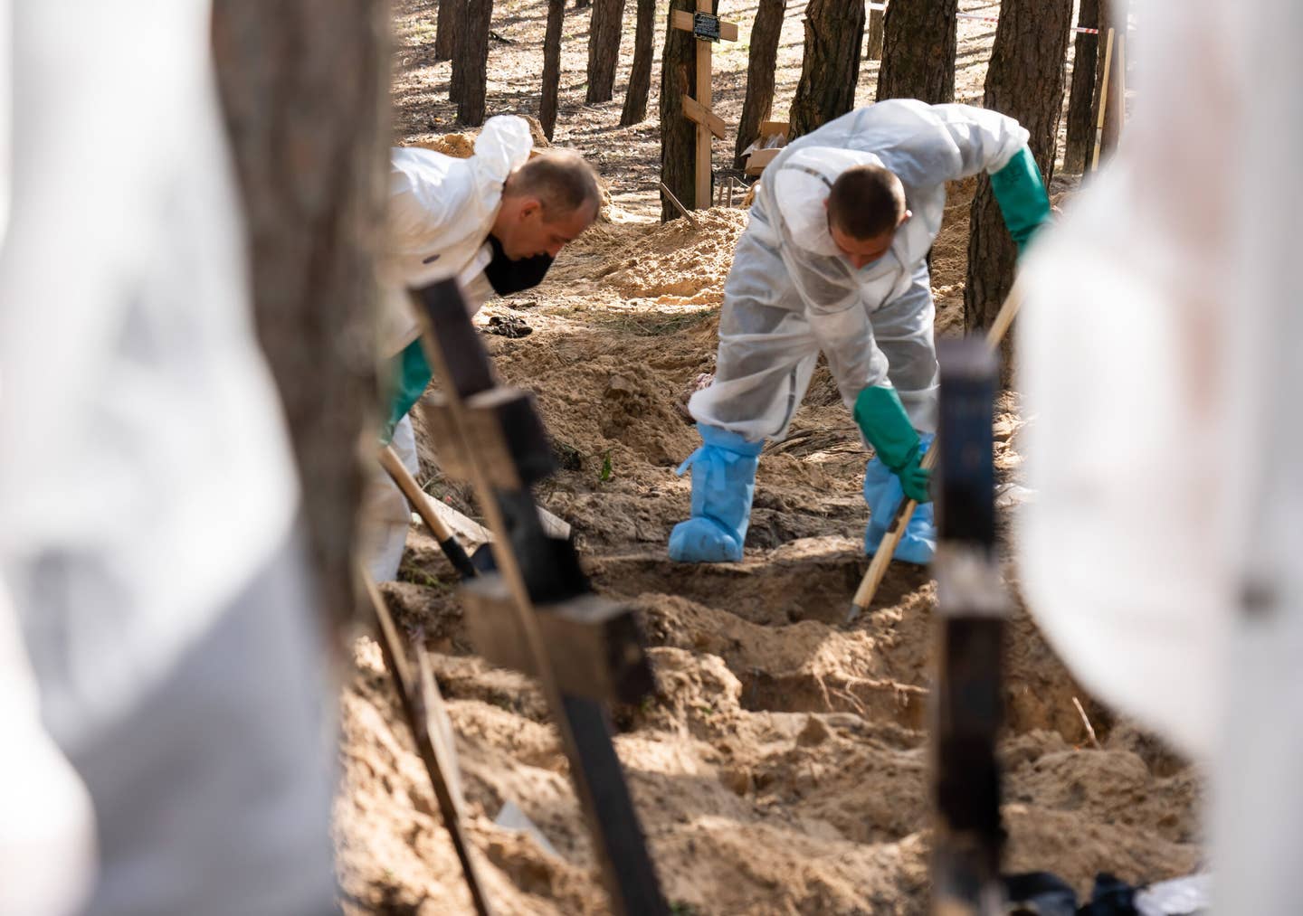 Investigators wearing protective gear are seen exhuming bodies with shovels. A mass burial site was found on the outskirt of the eastern Ukrainian city, Izium, Kharkiv region, which was liberated from Russian occupation. (Photo by Ashley Chan/SOPA Images/LightRocket via Getty Images)