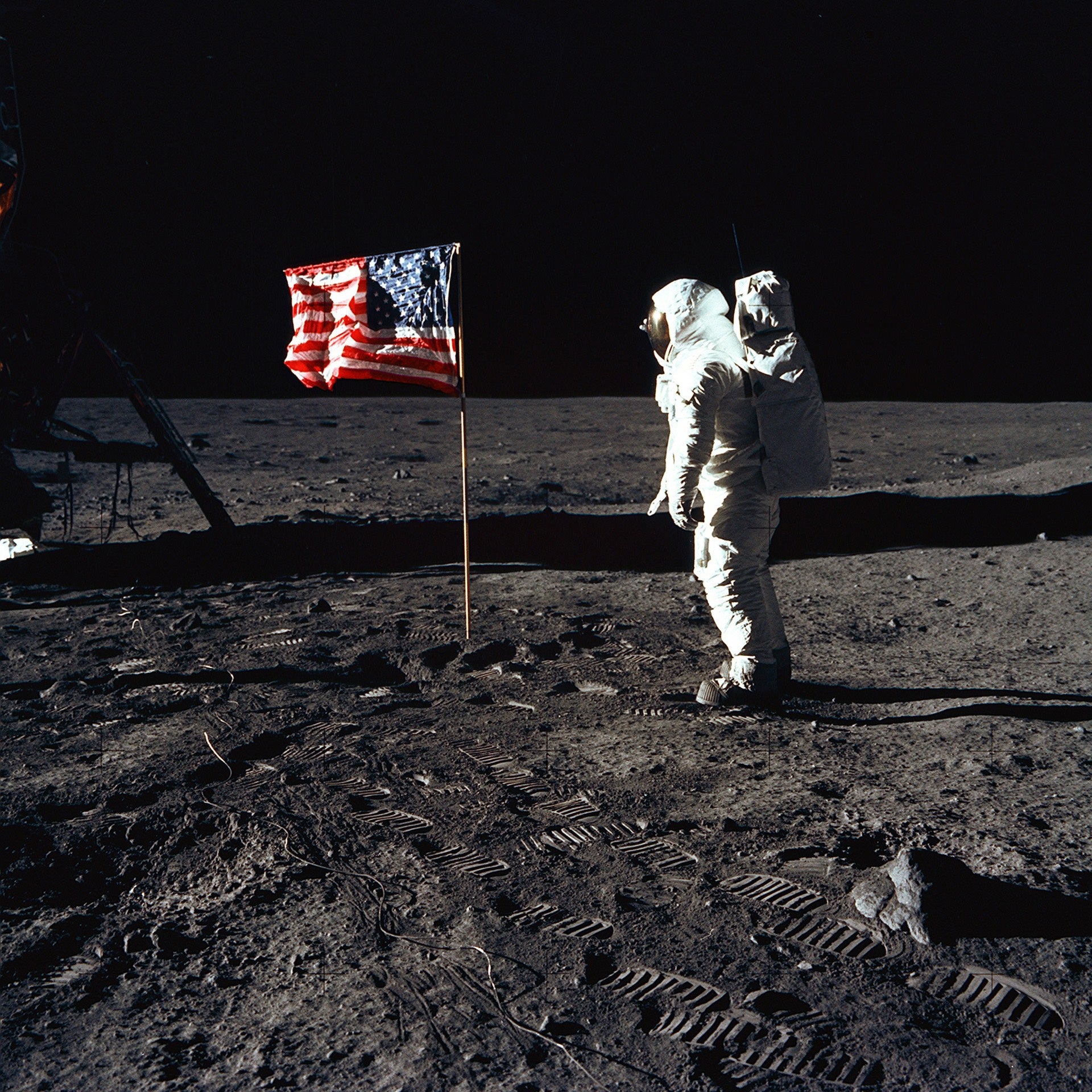 Astronaut Buzz Aldrin, lunar module pilot of the first lunar landing mission, poses for a photograph beside the deployed United States flag during an Apollo 11 Extravehicular Activity (EVA) on the lunar surface. The Lunar Module (LM) is on the left, and the footprints of the astronauts are clearly visible in the soil of the Moon. Astronaut Neil A. Armstrong, commander, took this picture with a 70mm Hasselblad lunar surface camera. While astronauts Armstrong and Aldrin descended in the LM, the "Eagle", to explore the Sea of Tranquility region of the Moon, astronaut Michael Collins, command module pilot, remained with the Command and Service Modules (CSM) "Columbia" in lunar-orbit.