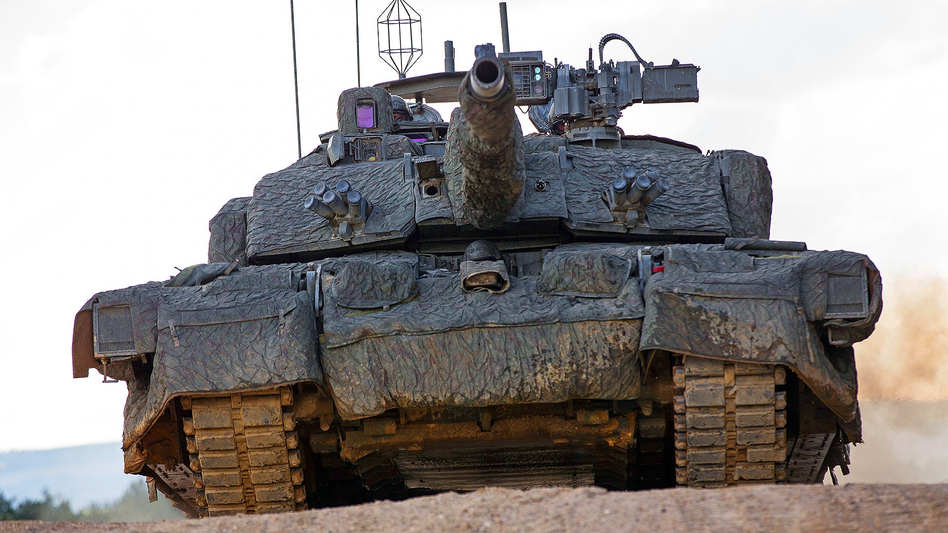 Pictured is the UK Main Battle Tank, Challenger 2 Theatre Entry Standard (CR2 TES) fitted with a Mobile Camouflage System (MCS). 

The tank is seen driving at high speed toward the camera.

This platform is the reference vehicle for the British Army and it is held at the Armoured Trials and Development Unit (ATDU) in Bovington. This tanks internal nickname is Megatron.

It is shown during testing at the Bovington test ground.