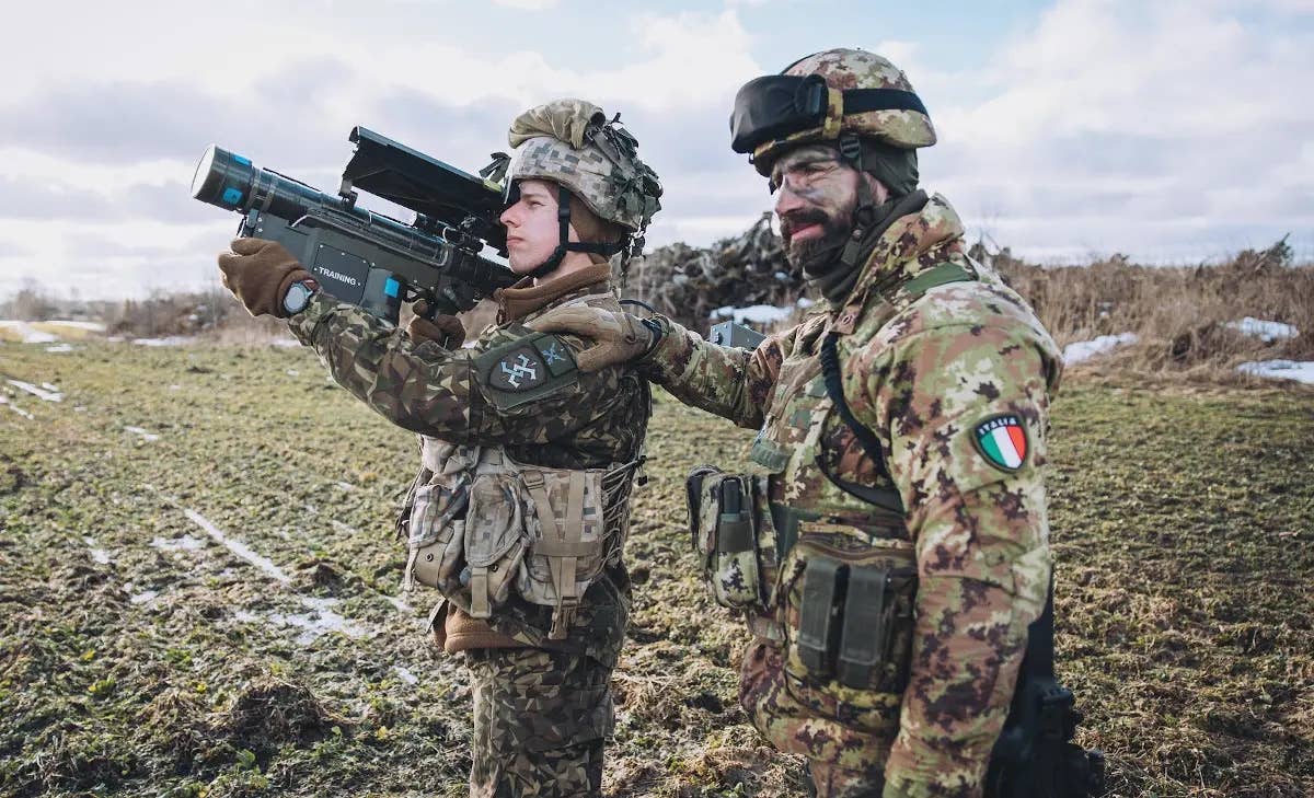 A member of the Latvia armed forces, left, holding a Stinger training launcher, stands with a member of the Italian military during a training exercise. <em>Latvia Armed Forces</em>