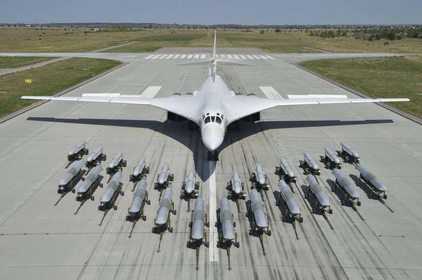 A row of 12 Kh-101/102-series air-launched cruise missiles, in front, and another dozen Kh-55-series missiles behind them, on display with a Tu-160 Blackjack bomber in the background. <em>Russian Ministry of Defense</em>