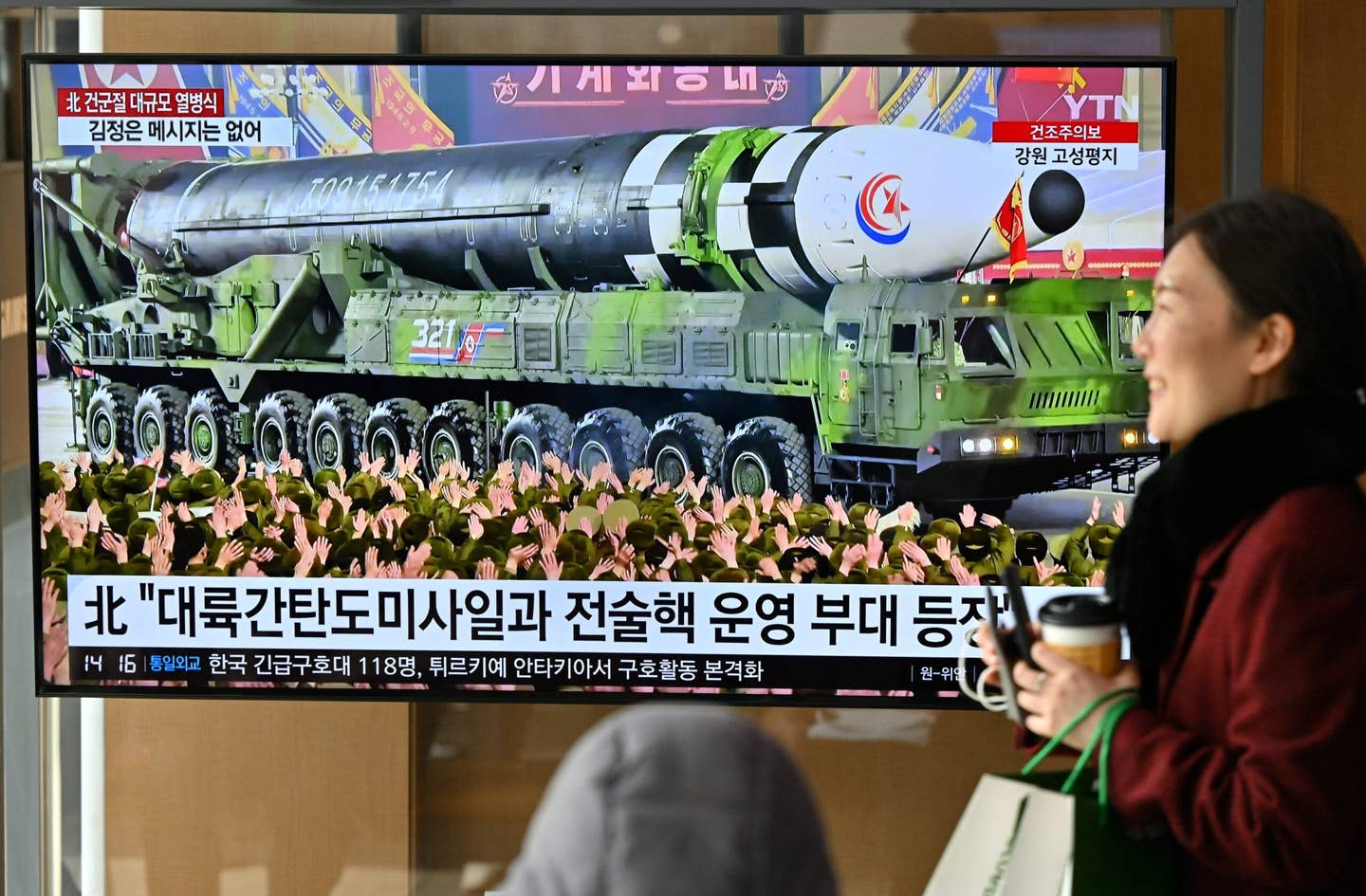 A woman walks past a television screen showing a news broadcast with an image of the North Korean military parade held in Pyongyang to mark the 75th founding anniversary of its armed forces, at a railway station in Seoul on February 9, 2023. <em>Photo by JUNG YEON-JE/AFP via Getty Images</em>