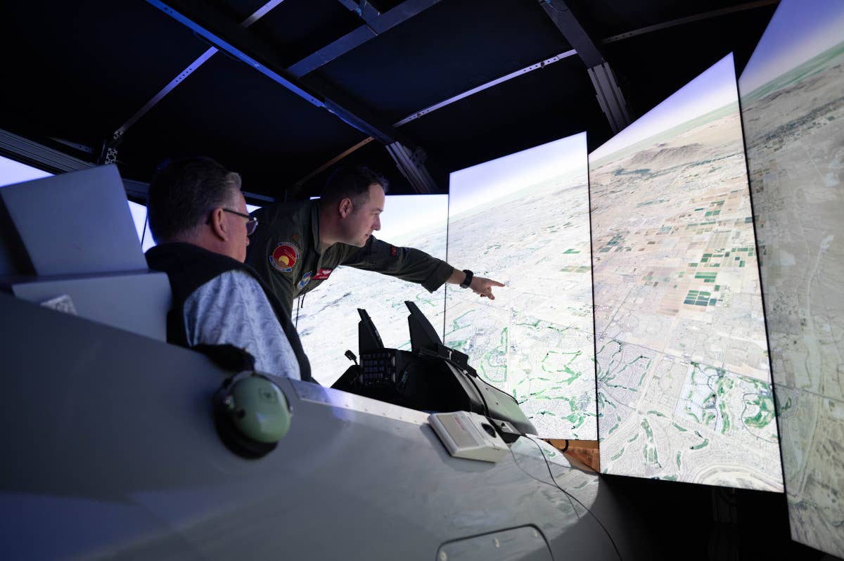 A member of the U.S. Air Force's 56th Fighter Wing talks to a civilian sitting in one type of F-16 fighter simulator during a community engagement event. <em>USAF</em>