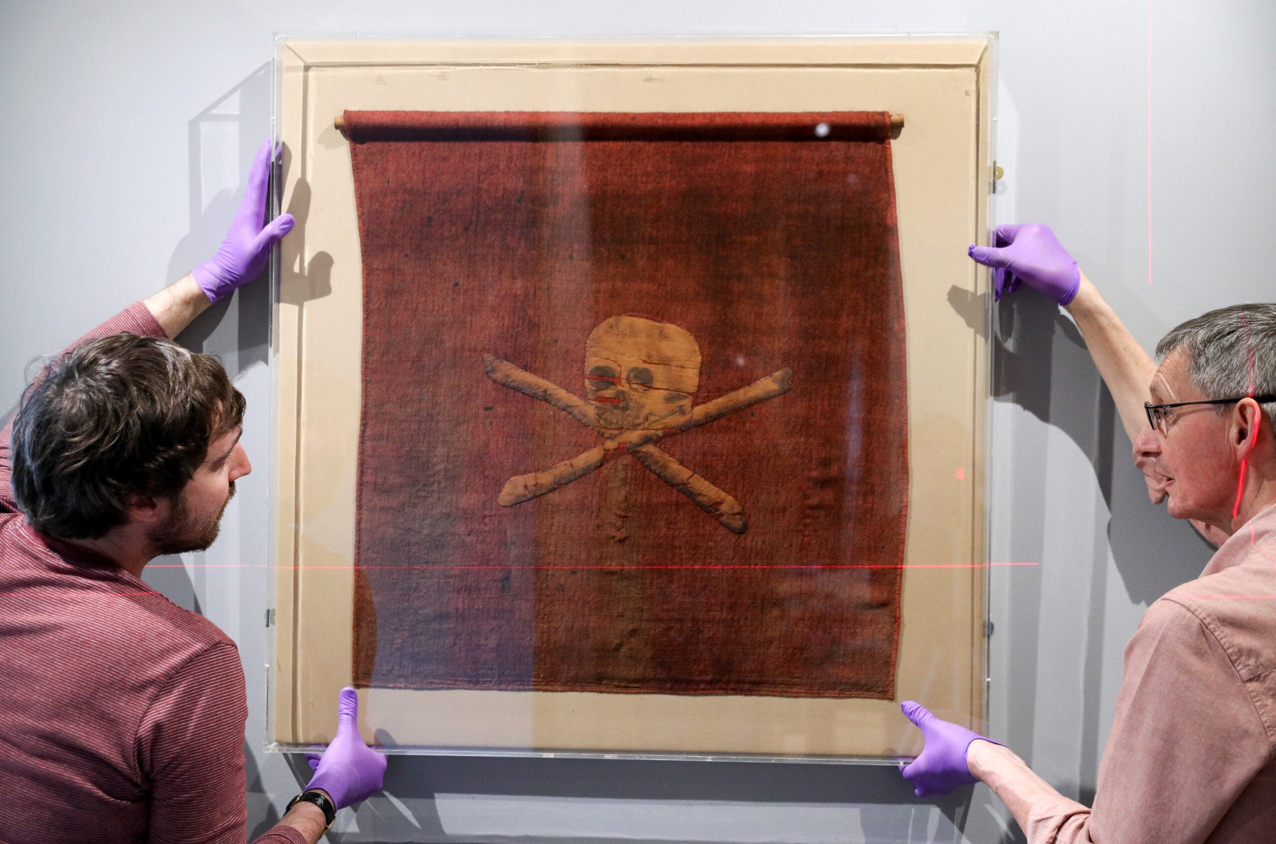 Exhibition staff at the National Museum of the Royal Navy, help hang a pirate flag which once belonged to Admiral Richard Curry, and was captured from pirates off the North African coast in 1790, during the preview of Jolly Roger: A Symbol of Terror and Pride exhibition at the National Museum of the Royal Navy at Portsmouth Historic Dockyard. (Photo by Andrew Matthews/PA Images via Getty Images)