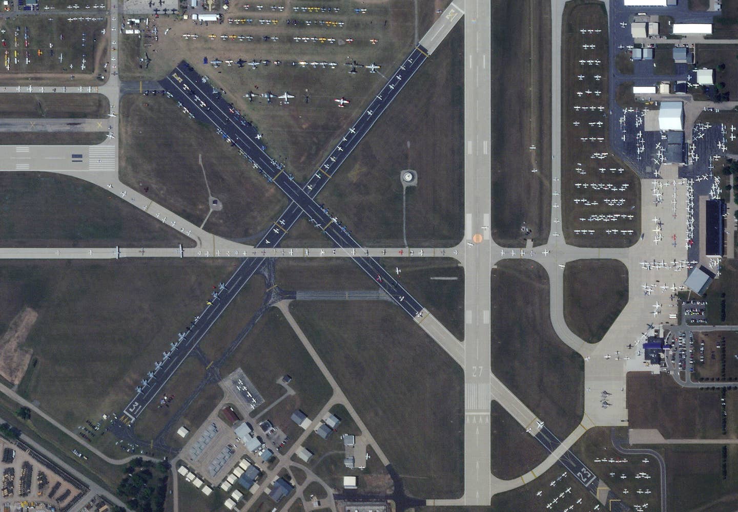 One end of the small cross runways turned into a hot pit area for tactical jets that would fly during the week. The F-22 demo team can be seen parked across the runway on another apron. Many of the jet warbirds are parked on the top left runway area. (<em>PHOTO © 2023 PLANET LABS INC. ALL RIGHTS RESERVED. REPRINTED BY PERMISSION</em>)