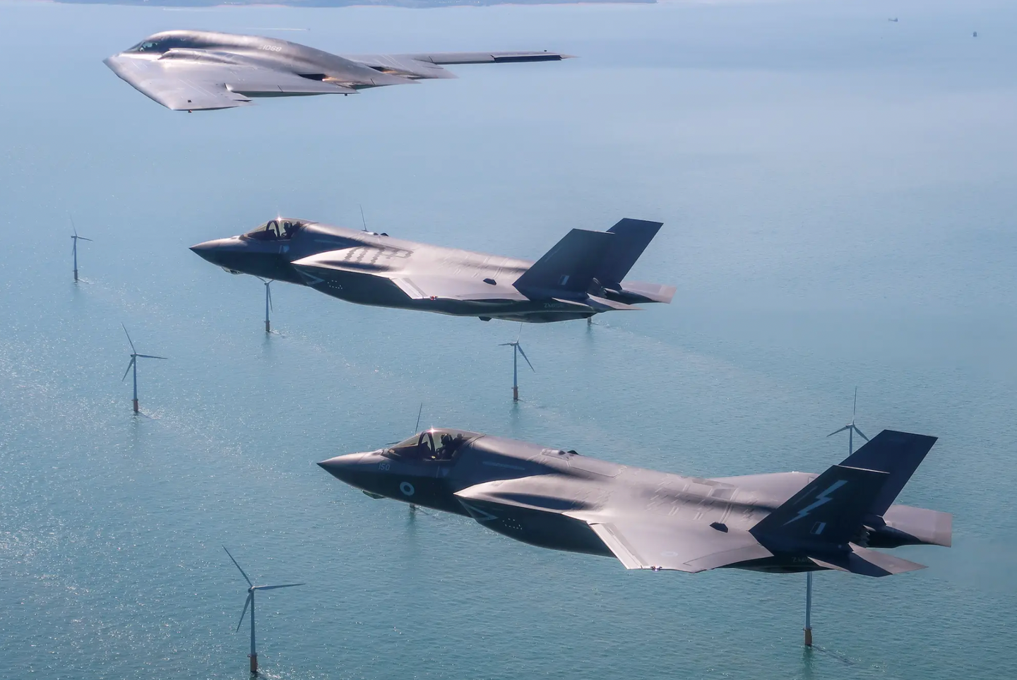 Two Royal Air Force F-35Bs (with ZM152 further from the camera) accompany a U.S. Air Force B-2 stealth bomber over the English coast during integration flying training in 2019.&nbsp;<em>Crown Copyright</em>