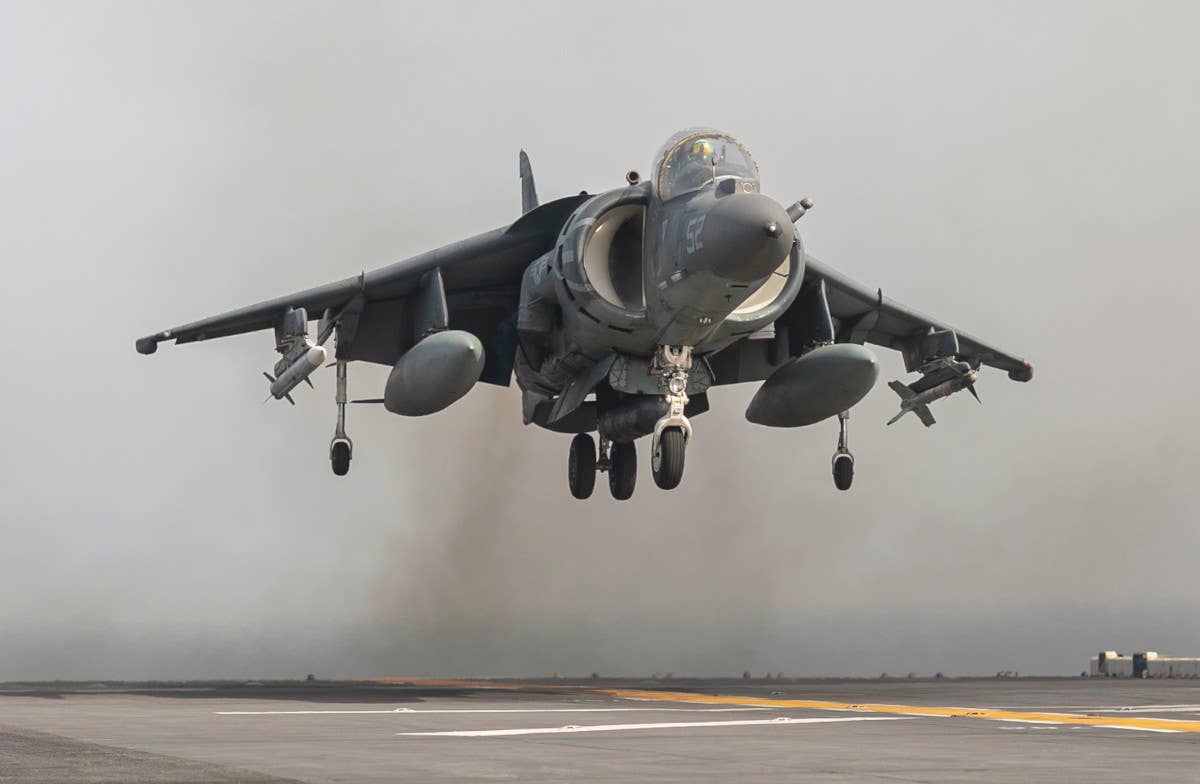 A Marine Corps AV-8B Harrier jump jet armed with one AIM-9M Sidewinder (under its left wing) and one AIM-120 AMRAAM (under its right wing) hovers over the deck of the US Bataan as it sails in the Gulf of Oman on August 14, 2023. <em>USMC</em>