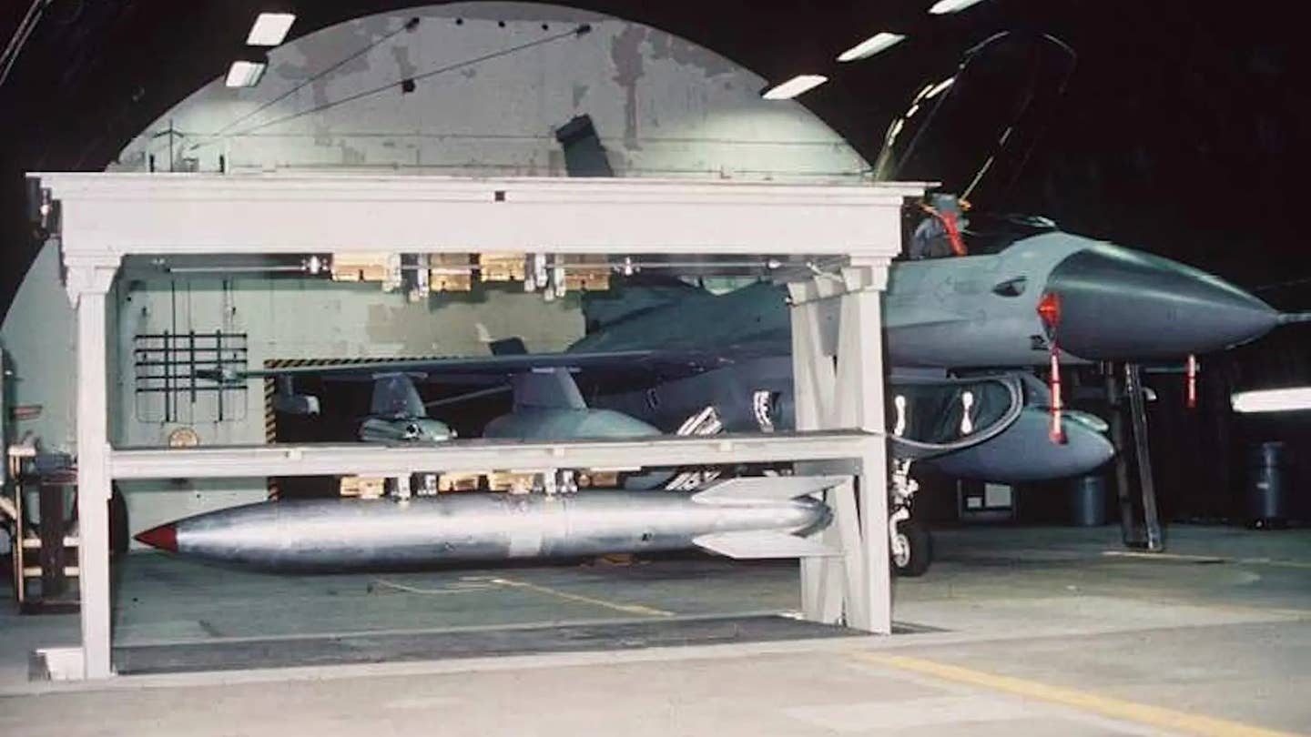 A B61 nuclear gravity bomb loaded into a special secure "vault" in a hangar somewhere in Europe. An F-16 Viper fighter is seen in the background. <em>DOD</em>
