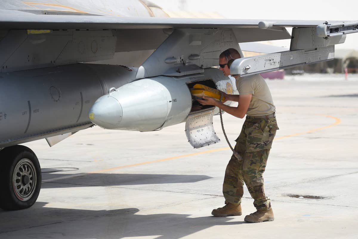 An airman loads chocks into the baggage pod under the wing of a US Air Force F-16. <em>USAF</em>