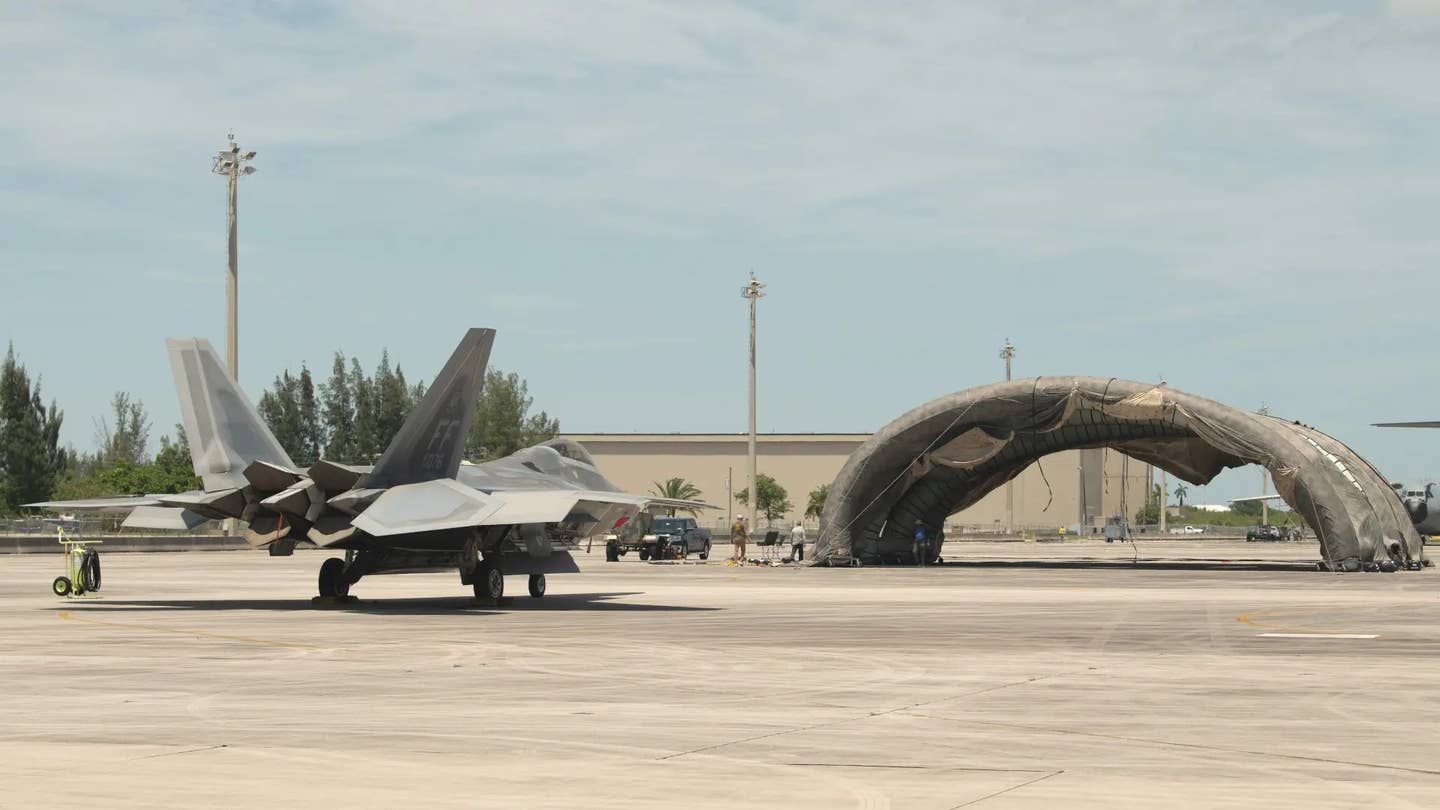 An F-22 sits in front of what was described as a "prototype portable camouflage, concealment, and deception hangar" at Homestead Air Reserve Base in Florida during Exercise Hoodoo Sea. <em>Air National Guard</em>