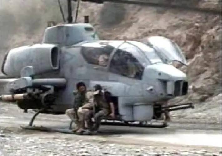 A Marine Corps AH-1W Super Cobra attack helicopter is used as an improvised transport in Afghanistan, with the personnel seen here riding on the helicopter's open ammunition bay door. <em>Public domain</em>