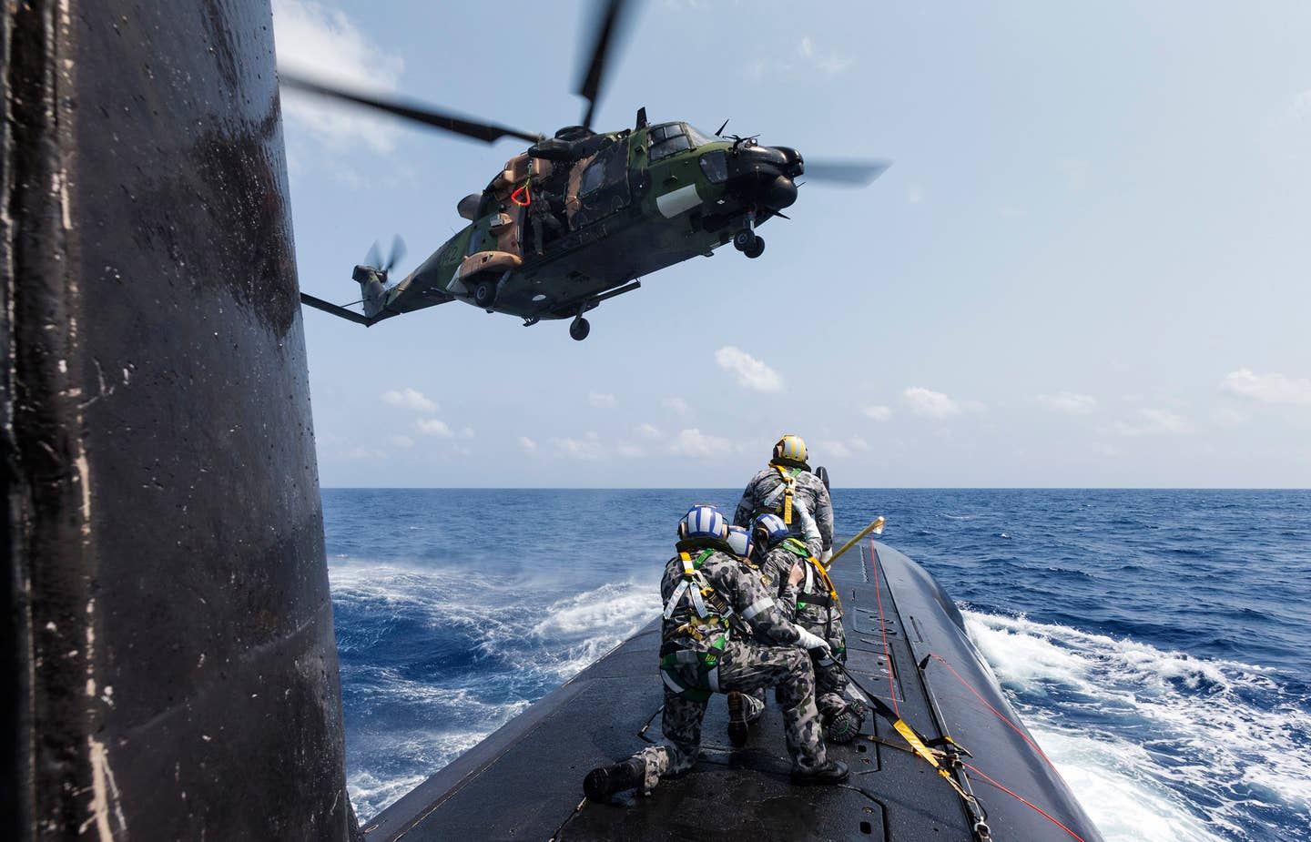 A team of Royal Australian Navy submariners on board HMAS <em>Collins</em> await a winch from an MRH90 helicopter during a personnel transfer while sailing in the Bay of Bengal as part of AUSINDEX 2019. <em>COMMONWEALTH OF AUSTRALIA, DEPARTMENT OF DEFENSE</em>