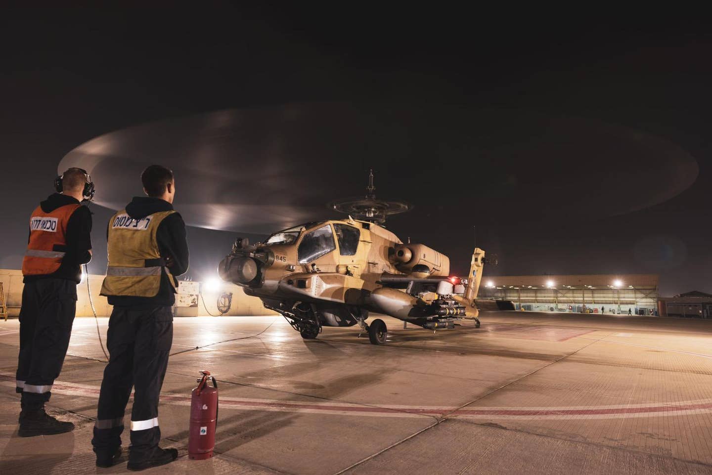 A night-time view of an AH-64A with the gray-painted avionics pod fitted below the fuselage. <em>IAF</em>