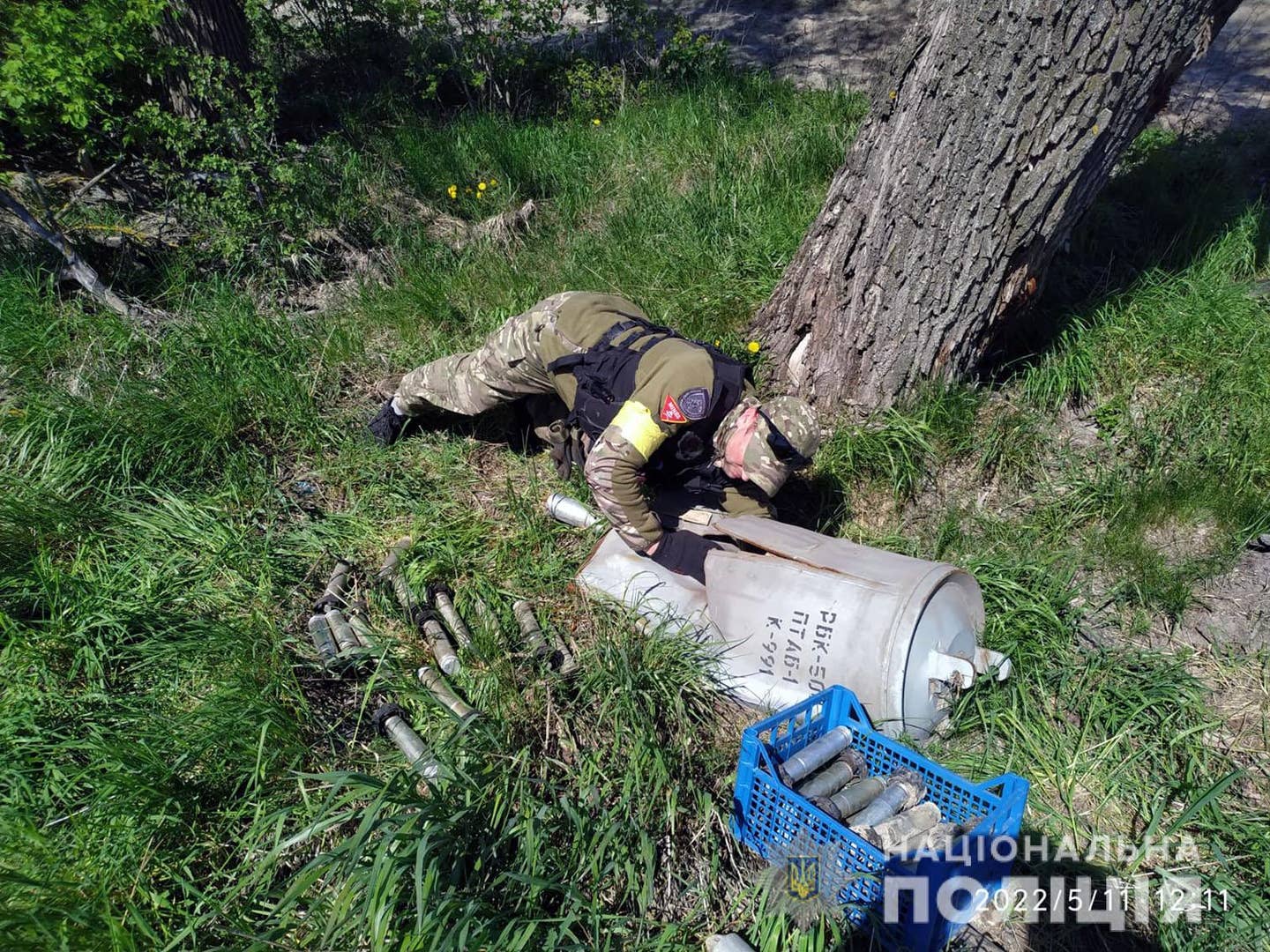 A member of the Ukrainian police collects and disposes the remains of a Russian RBK-500 cluster bomb together with the PTAB-1M anti-tank cluster bomblets it contained. This was found in the Chernihiv region of Ukraine on May 11, 2022. <em>National Police of Ukraine</em>