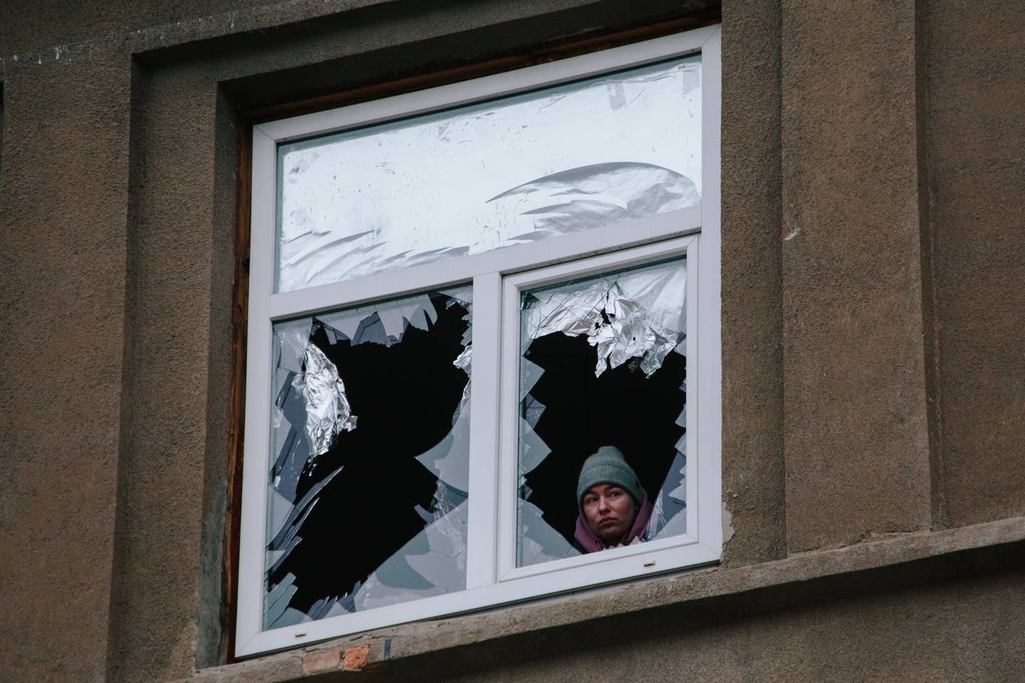 A woman is looking out of a window that has been broken by an explosion, in Kharkiv, Ukraine, on December 8, 2023. <em>Photo by Pavlo Pakhomenko/NurPhoto via Getty Images</em>
