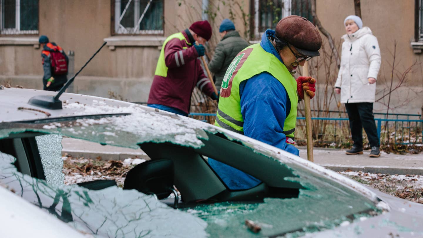 Utility workers are cleaning up the aftermath of an attack against the backdrop of a damaged car, in Kharkiv, Ukraine, on December 8, 2023.