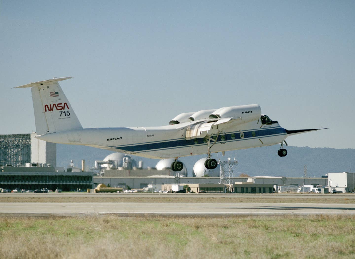 Seen in better days, the QSRA takes off in front of the NASA Ames National Full-Scale Aerodynamic Facility (a 40-by-80-by-120-foot wind tunnel and Outdoor Aerodynamic Research Facility) during the dedication of the facility in 1987. <em>NASA</em>