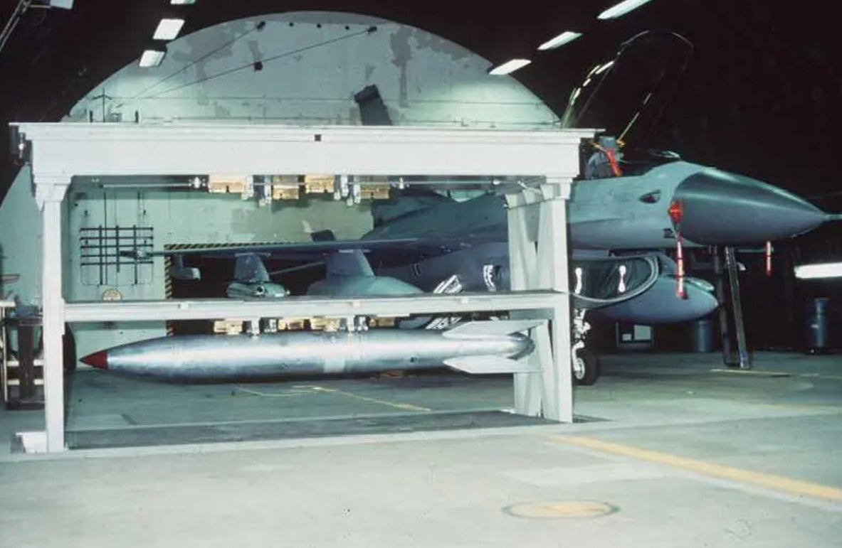 A Weapons Storage and Security System vault in raised position holding an earlier model of B61 nuclear bomb. The vault is within a Protective Aircraft Shelter. Public Domain/WikiCommons 
