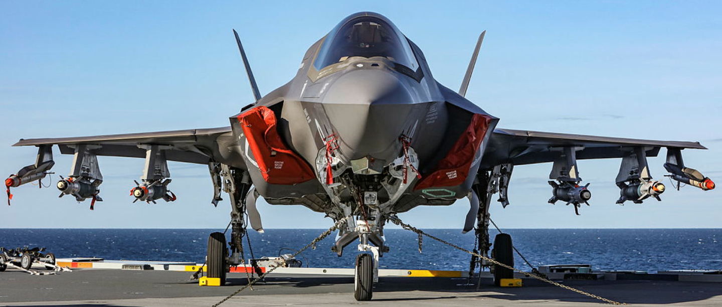 A fully loaded UK F-35B on the deck of HMS <em>Queen Elizabeth</em>. Stores on the underwing stations include four 500-pound Paveway IV precision-guided bombs. <em>Crown Copyright</em>