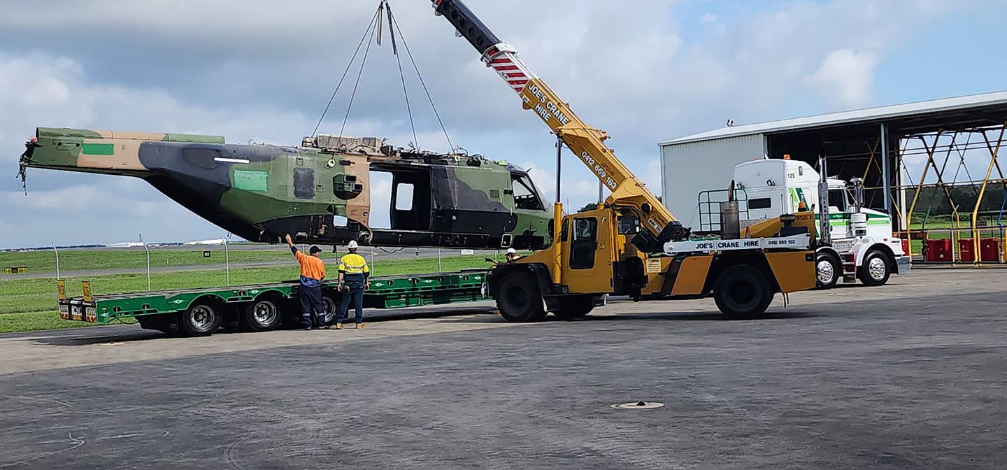 A completely stripped and cannibalized Australian Army NH-90 helicopter is craned onto a semi trailer at Airbus Australia Pacific’s facility for transport to Amberley and burial. <em>Picture undisclosed</em>