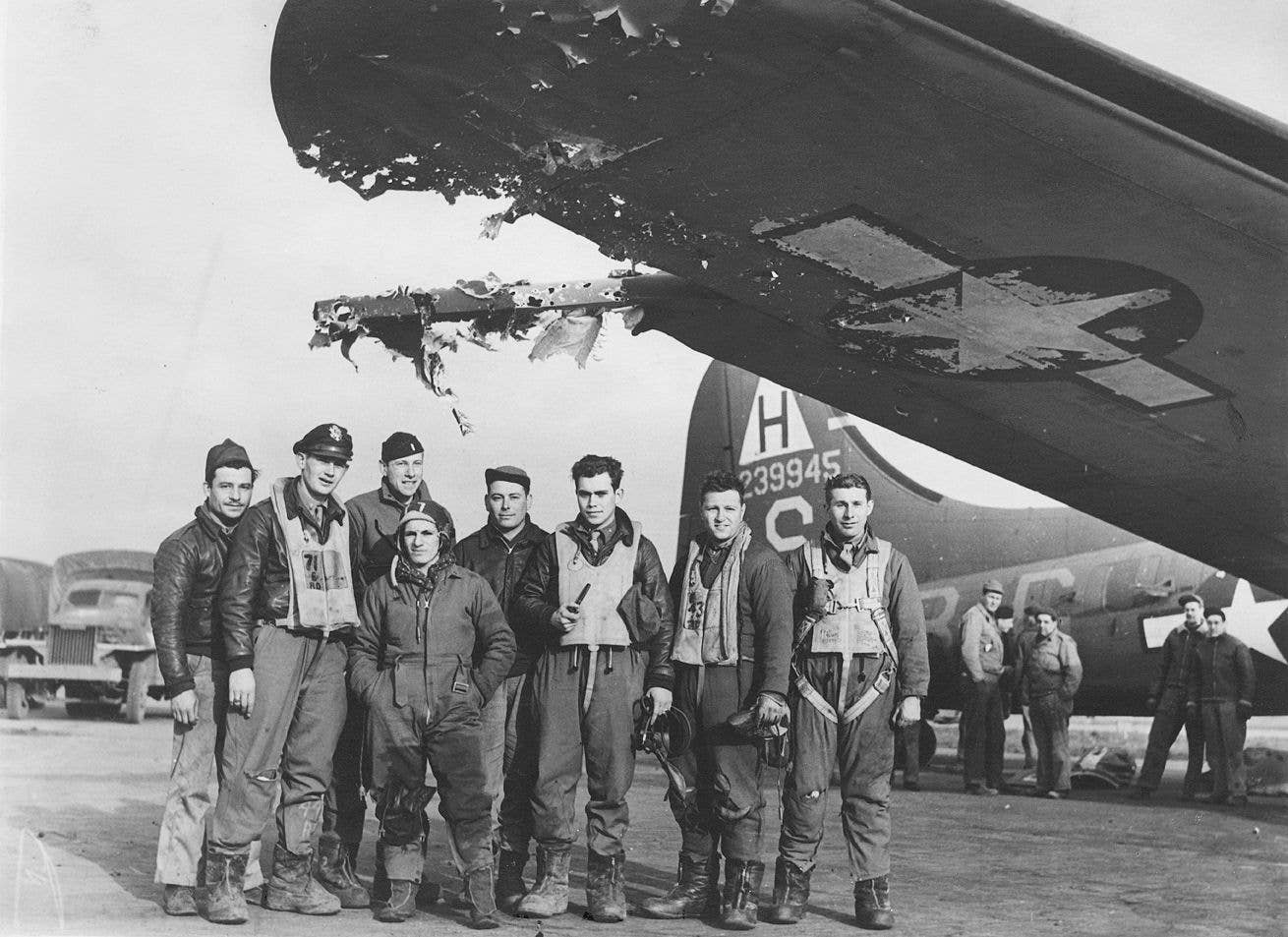 A B-17 crew of the 306th Bomb Group stand underneath the flak-damaged wing of their B-17, nicknamed <em>Holy</em> <em>Hellcat</em>, in 1943. <em>United States Army Air Forces</em>