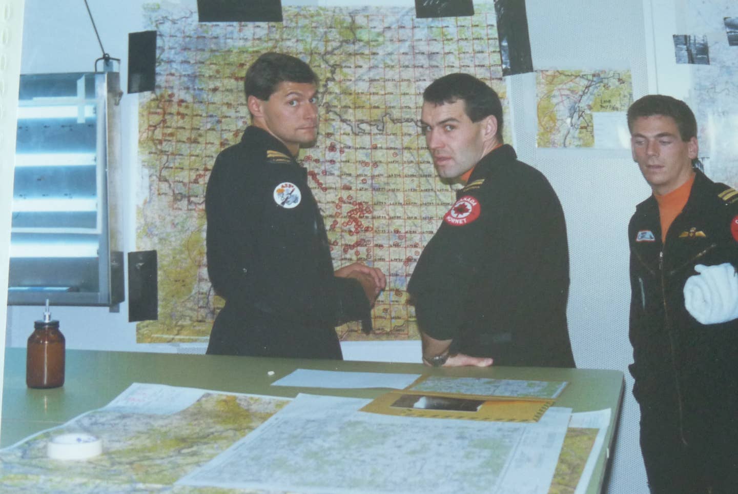 Pilots from 433 Squadron in their deployed bunker, Lahr, West Germany. Today's mission lead, Dog, has a towel under his arm. The planning map behind the two other pilots clearly shows the inter-German border. <em>Dan McWilliams</em>