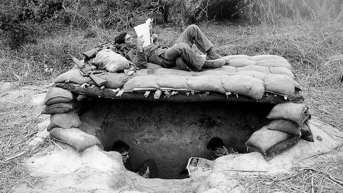 U.S. soldiers take time out to read newspapers and magazines above and below their sandbagged bunker in a base camp set up in a jungle clearing in South Vietnam near the Cambodian border on November 28, 1966. AP Photo/Horst Faas.