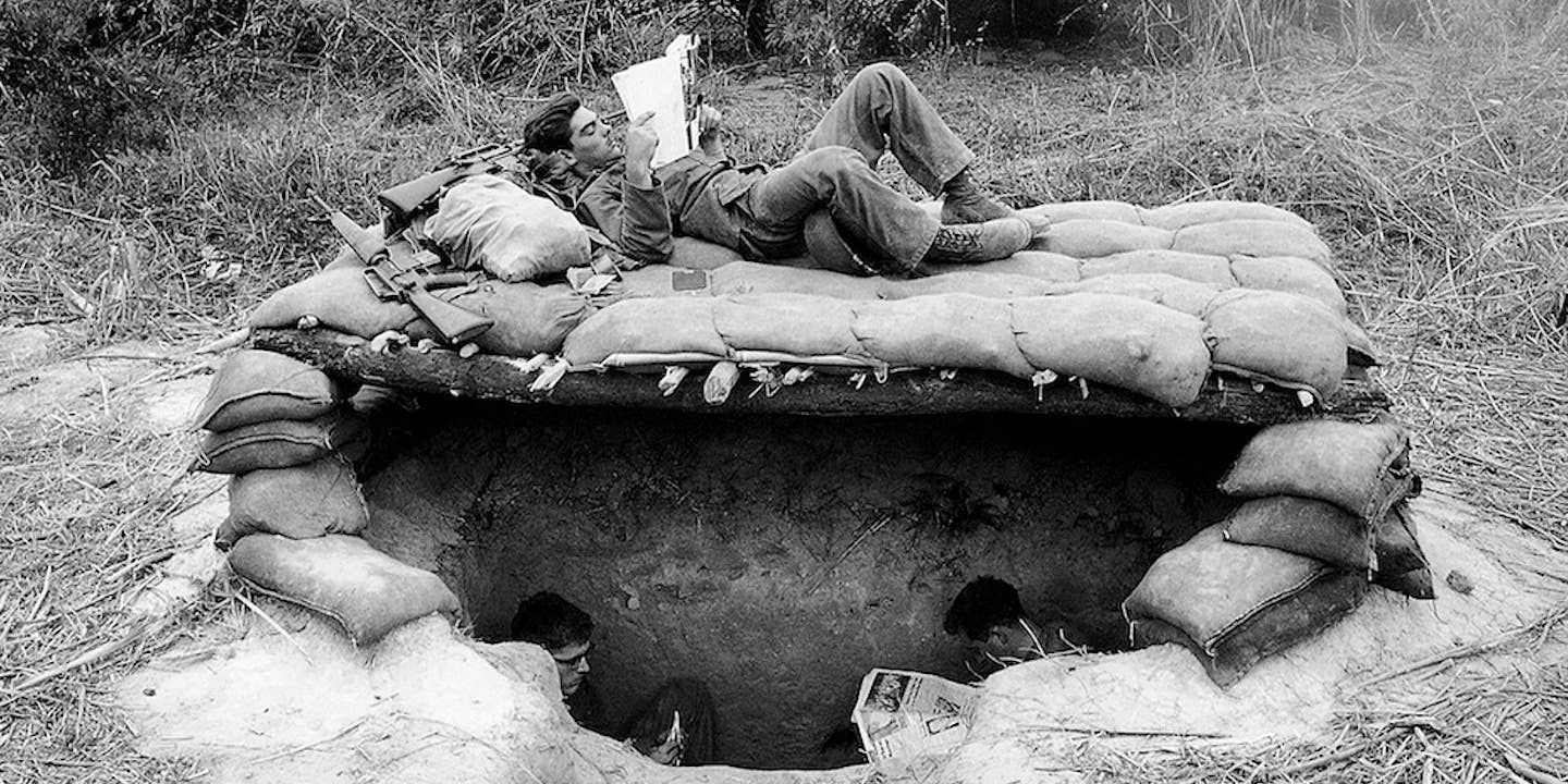U.S. soldiers take time out to read newspapers and magazines above and below their sandbagged bunker in a base camp set up in a jungle clearing in South Vietnam near the Cambodian border on November 28, 1966. AP Photo/Horst Faas.