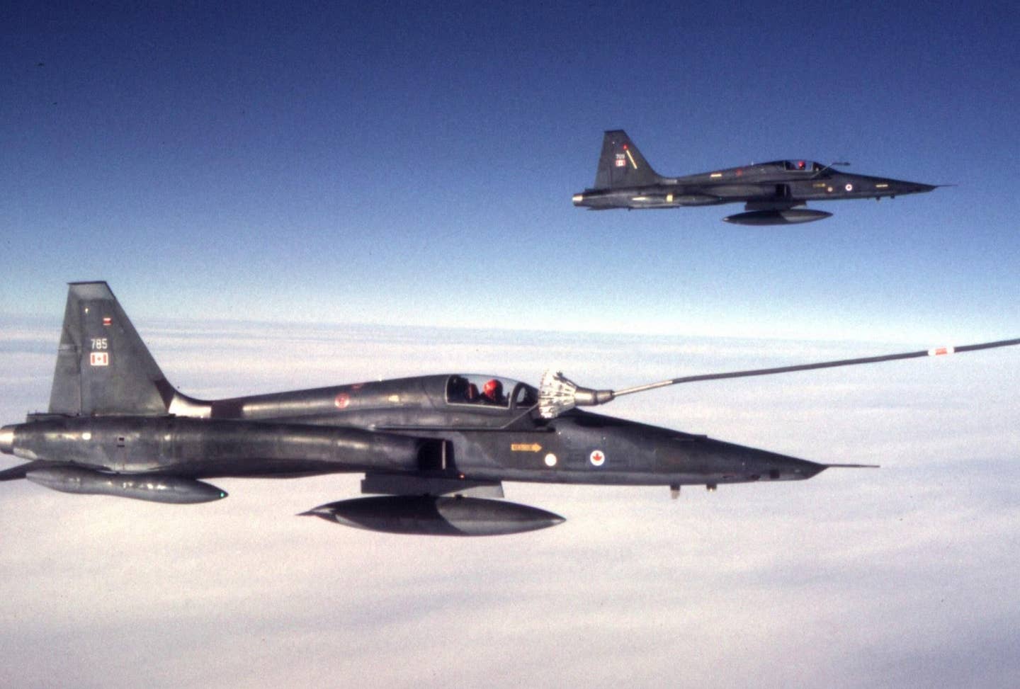 A CF-5 receiving fuel from a Boeing 707 tanker, with undercast clouds below. The pilot’s helmet is orange, the colors of 433 Squadron.<em> Dan McWilliams</em>
