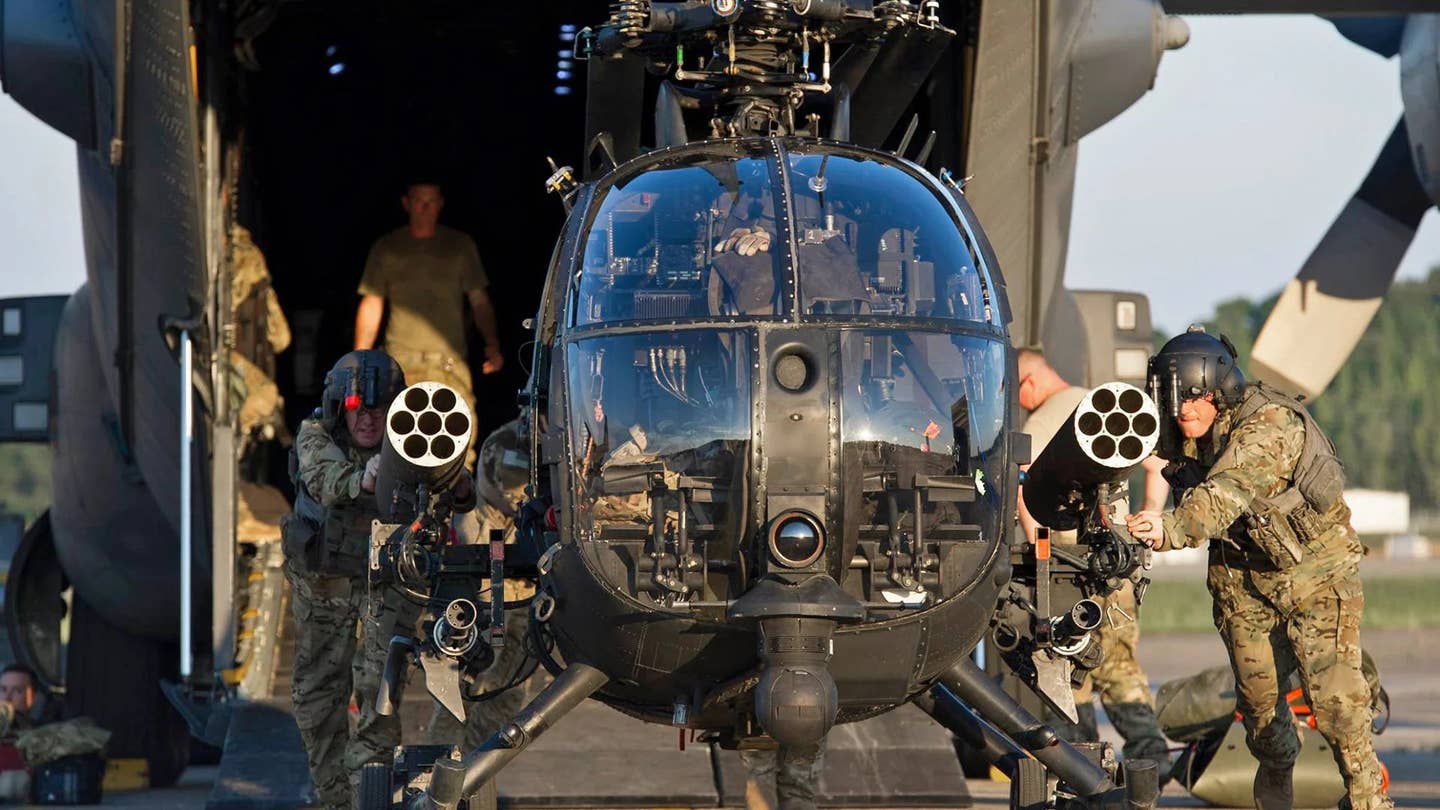 An AH-6M Little Bird is seen here being unloaded from a C-130-series aircraft. Note the upturned rocket pods and the folded main rotor, which help reduce the helicopter's physical size for ease of transport. <em>DOD</em>