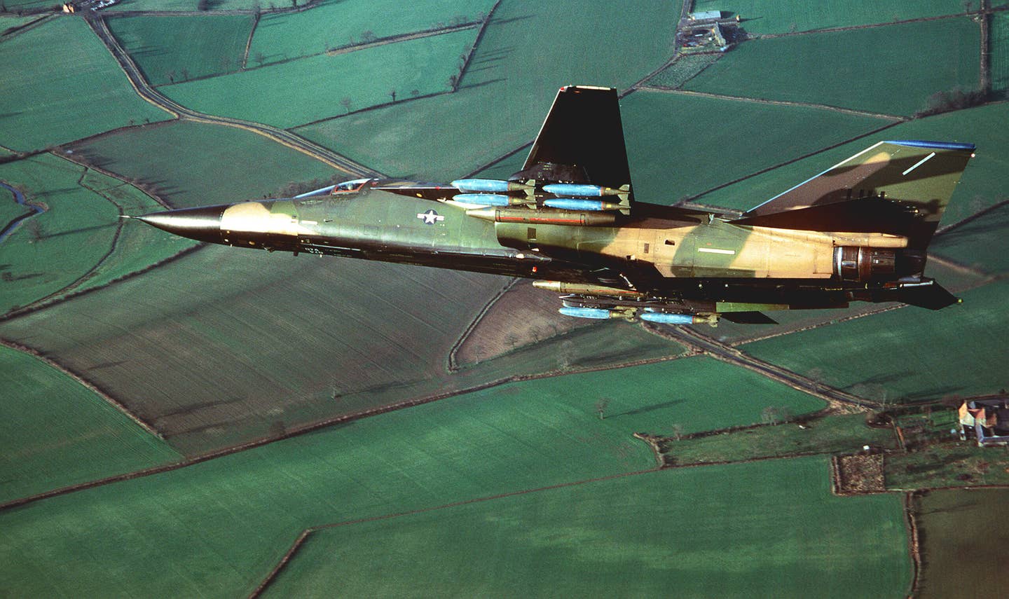 An air-to-air view of an F-111 flown by the 20th Tactical Fighter Wing at RAF Upper Heyford carrying a full load of bombs on its wing pylons, circa 1983. <em>U.S. Air Force</em>
