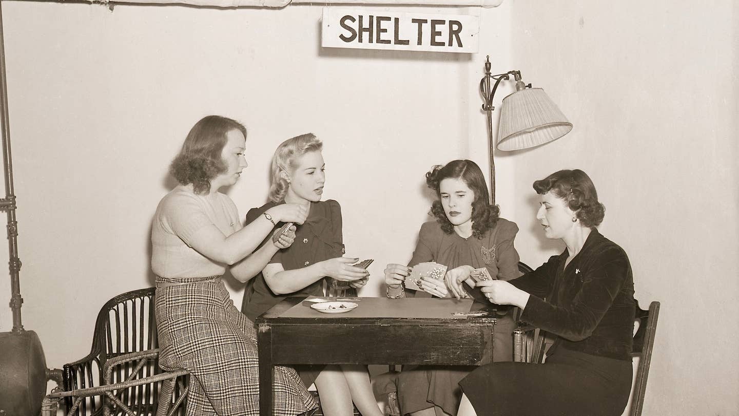 3/12/1941- New York, NY: Hotel completes air raid shelter. A few of the Allerton House's guests showed how comfortable and practical are the conveniences incorporated in the new air-raid shelter completed in the sub-basement of the hotel. The shelter is approximately 45 feet underground, and an auxiliary lighting system has been installed in case the hotel's own light plant goes out of order. This photo shows four women happily playing cards under a sign that says "Shelter." Bettmann via Getty Images.