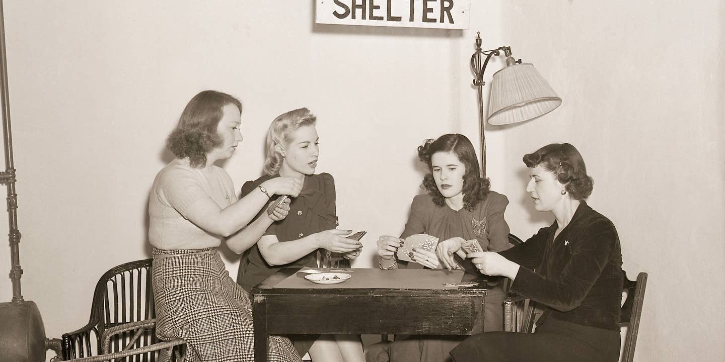 3/12/1941- New York, NY: Hotel completes air raid shelter. A few of the Allerton House's guests showed how comfortable and practical are the conveniences incorporated in the new air-raid shelter completed in the sub-basement of the hotel. The shelter is approximately 45 feet underground, and an auxiliary lighting system has been installed in case the hotel's own light plant goes out of order. This photo shows four women happily playing cards under a sign that says "Shelter." Bettmann via Getty Images.