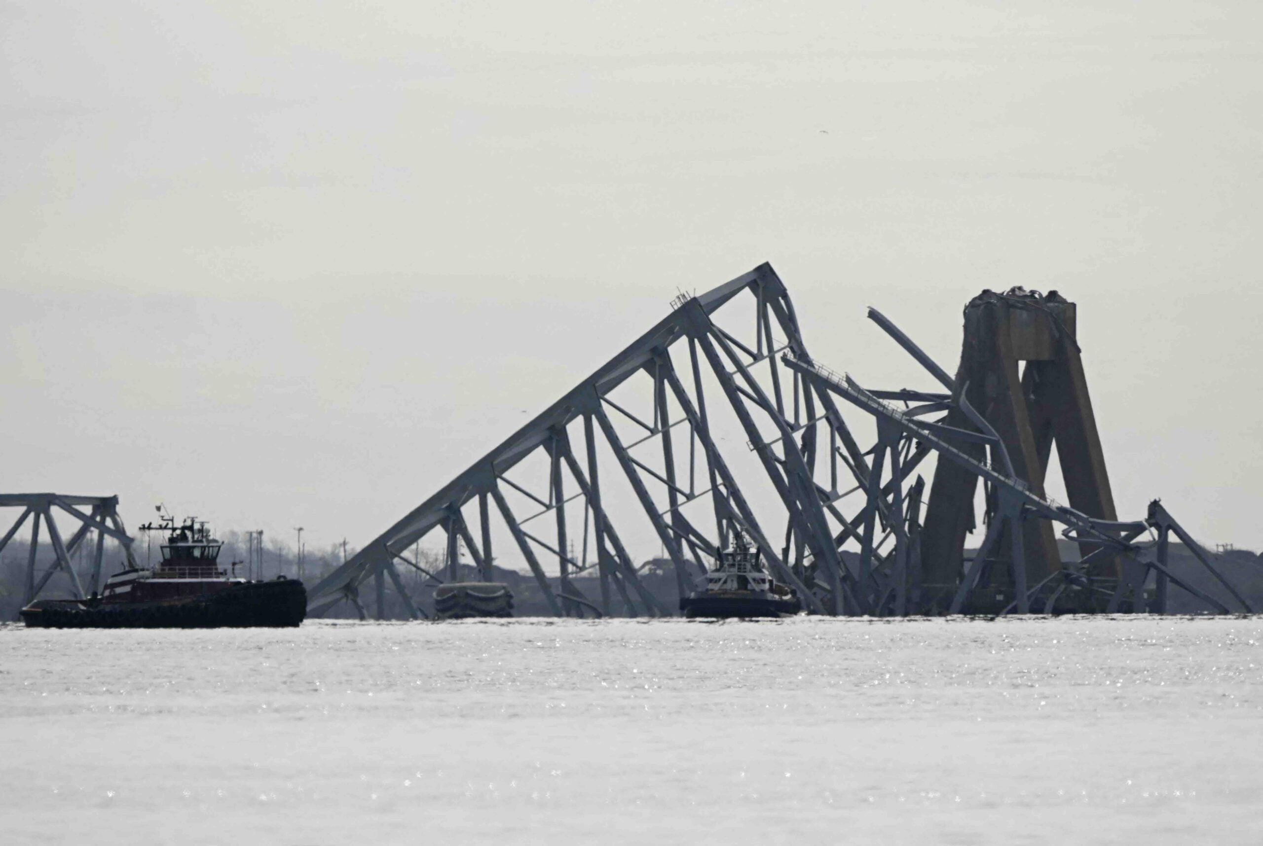 The steel frame of the Francis Scott Key Bridge lies in the water after it collapsed in Baltimore, Maryland, on March 26, 2024. The bridge collapsed early March 26 after being struck by the Singapore-flagged Dali container ship, sending multiple vehicles and people plunging into the frigid harbor below. There was no immediate confirmation of the cause of the disaster, but Baltimore's Police Commissioner Richard Worley said there was "no indication" of terrorism. (Photo by Mandel NGAN / AFP)