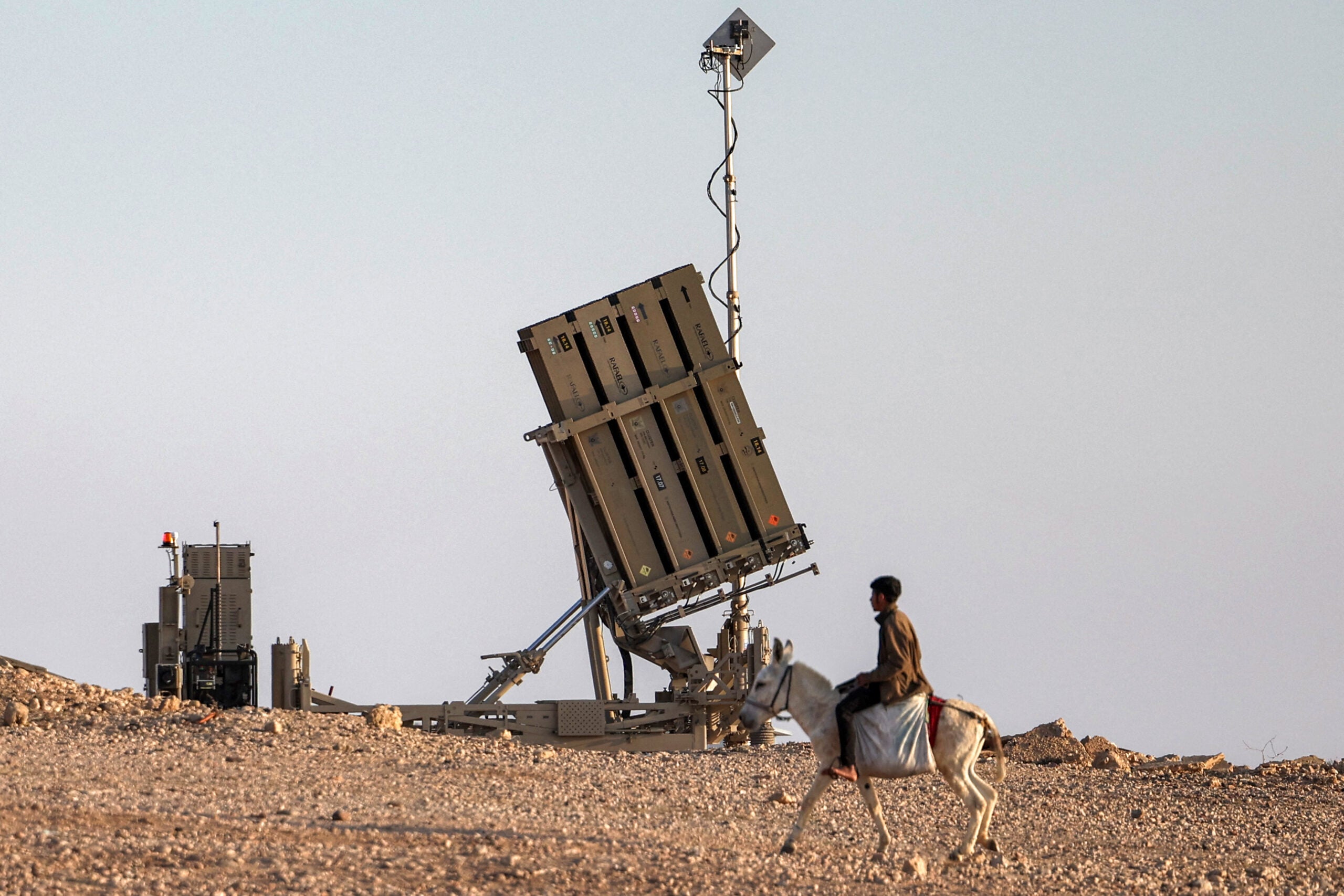 TOPSHOT - A boy rides a donkey near one of the batteries of Israel's Iron Dome missile defence system at a village not recognised by Israeli authorities in the southern Negev desert on April 14, 2024. (Photo by AHMAD GHARABLI / AFP) (Photo by AHMAD GHARABLI/AFP via Getty Images)
