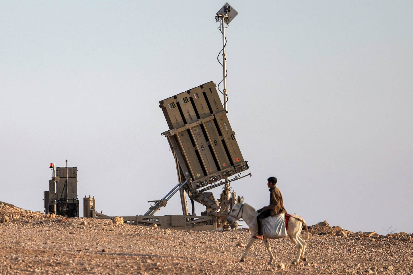 A boy rides a donkey near one of the batteries of the Israeli Iron Dome missile defense system at a village not recognized by Israeli authorities in the southern Negev desert on April 14, 2024. <em>Photo by AHMAD GHARABLI/AFP via Getty Images</em>
