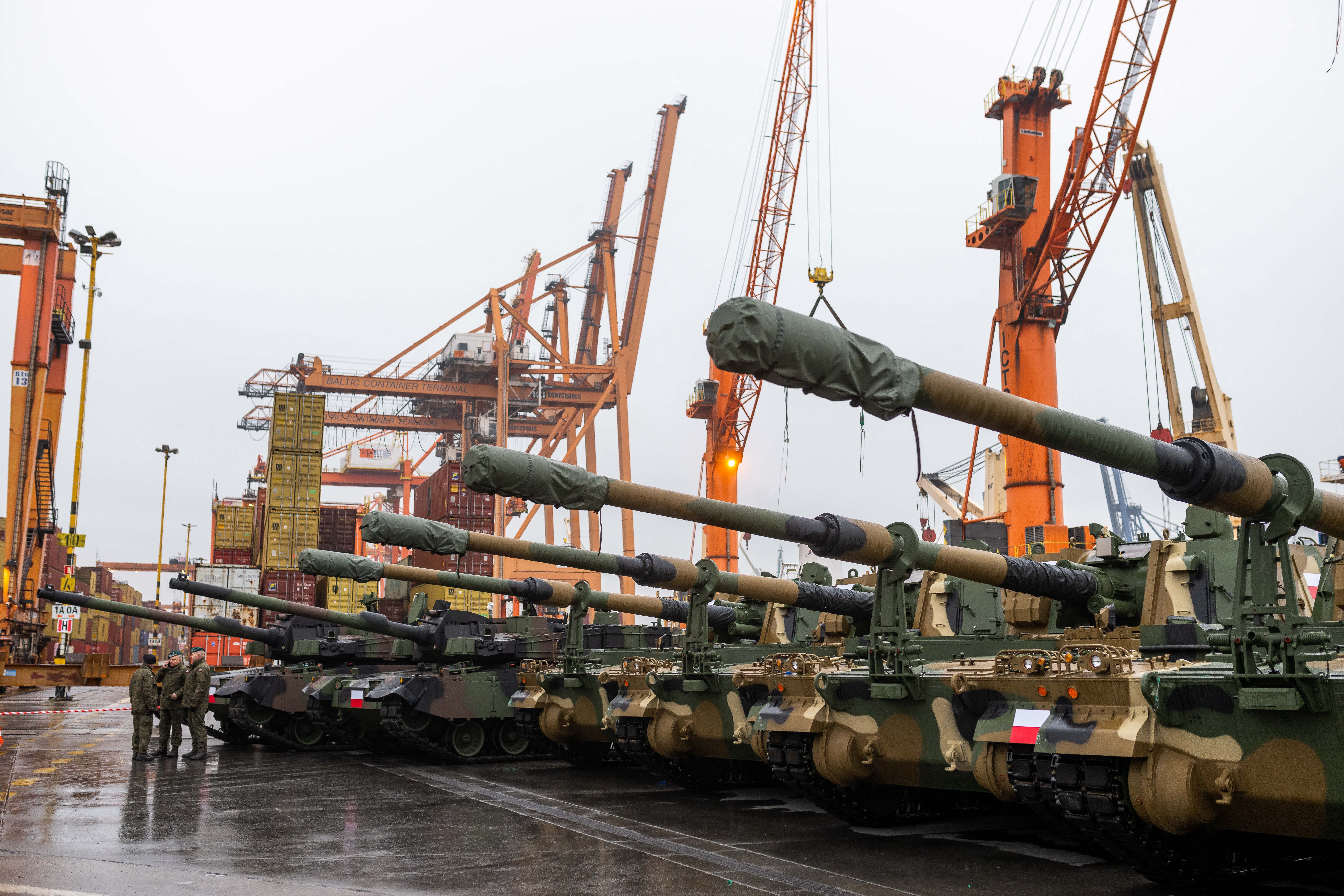 Polish Army soldiers stand in front of army equipment in the port after the arrival of the first K2 tanks and K9 howitzers for Poland on December 6, 2022 at the Baltic Container Terminal in Gdynia. - The Polish Army is strengthening its potential with the use of South Korean defense technologies. In July 2022 an agreement was concluded with Hyundai Rotem for the acquisition of a total of 1,000 K2 tanks with accompanying vehicles. Poland has massively stepped up weapons purchases since Russia invaded Ukraine, as well as sending military aid to Kyiv and taking in millions of Ukrainian refugees. (Photo by MATEUSZ SLODKOWSKI / AFP) (Photo by MATEUSZ SLODKOWSKI/AFP via Getty Images)