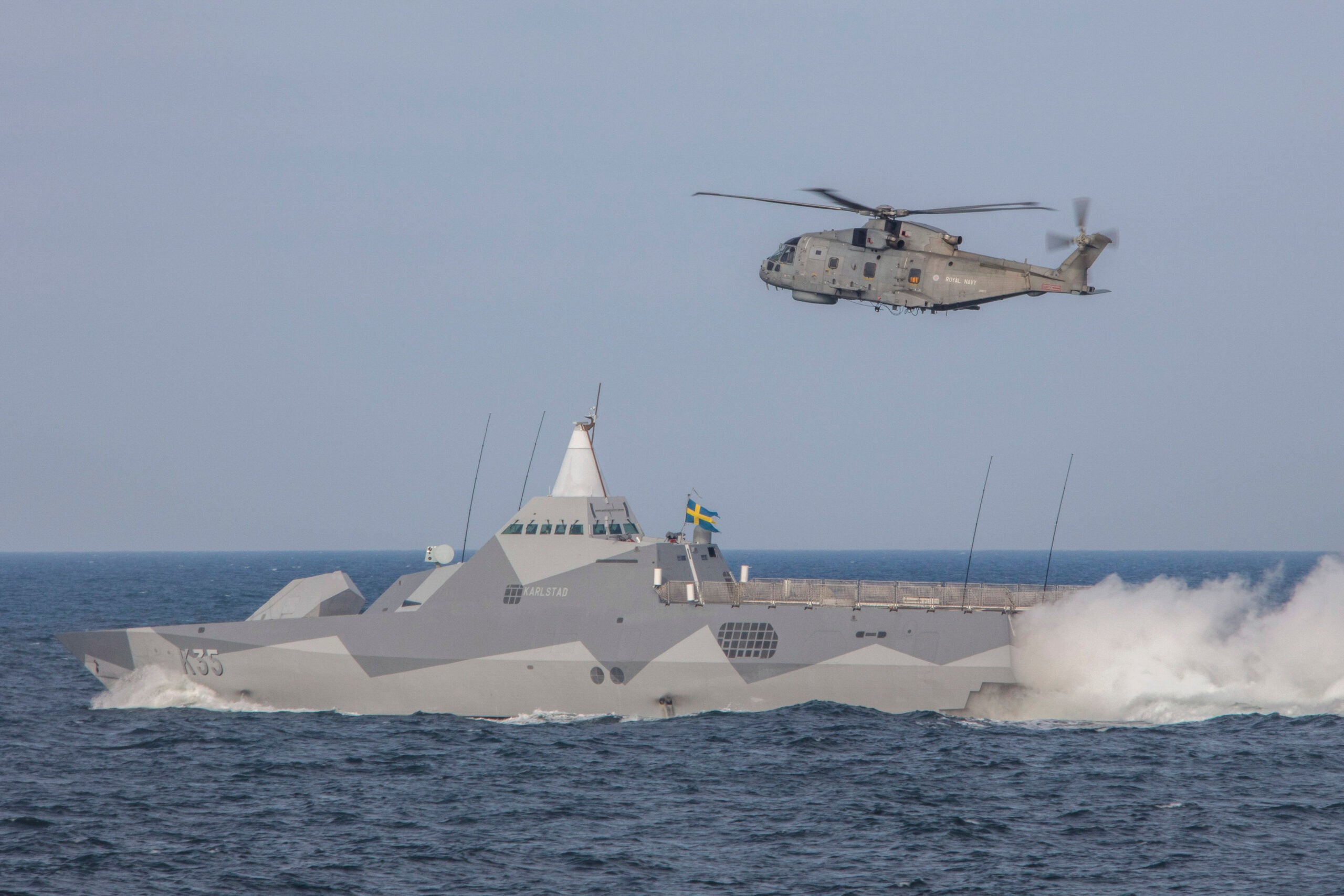 Pictured are Swedish Corvette HSwMS Karlstad and Royal Navy Merlin helicopter taking part in a surface exercise with partnering NATO warships whilst participating in BALTOPS 20.

On Friday 12th June 2020, Royal Navy ships took part in a surface engagement exercise (SURFEX) with NATO ships whilst on BALTOPS 20.

The NATO exercise which takes place each year will see various countries take part in gunnery serials, man overboard exercises, air defence and anti-submarine exercises, and not to mention close proximity sailing.

The Visby class is the latest class of corvette to be adopted by the Swedish Navy after the Göteborg and Stockholm-class corvettes. 

The ship's design heavily emphasizes low visibility, radar cross-section and infrared signature.