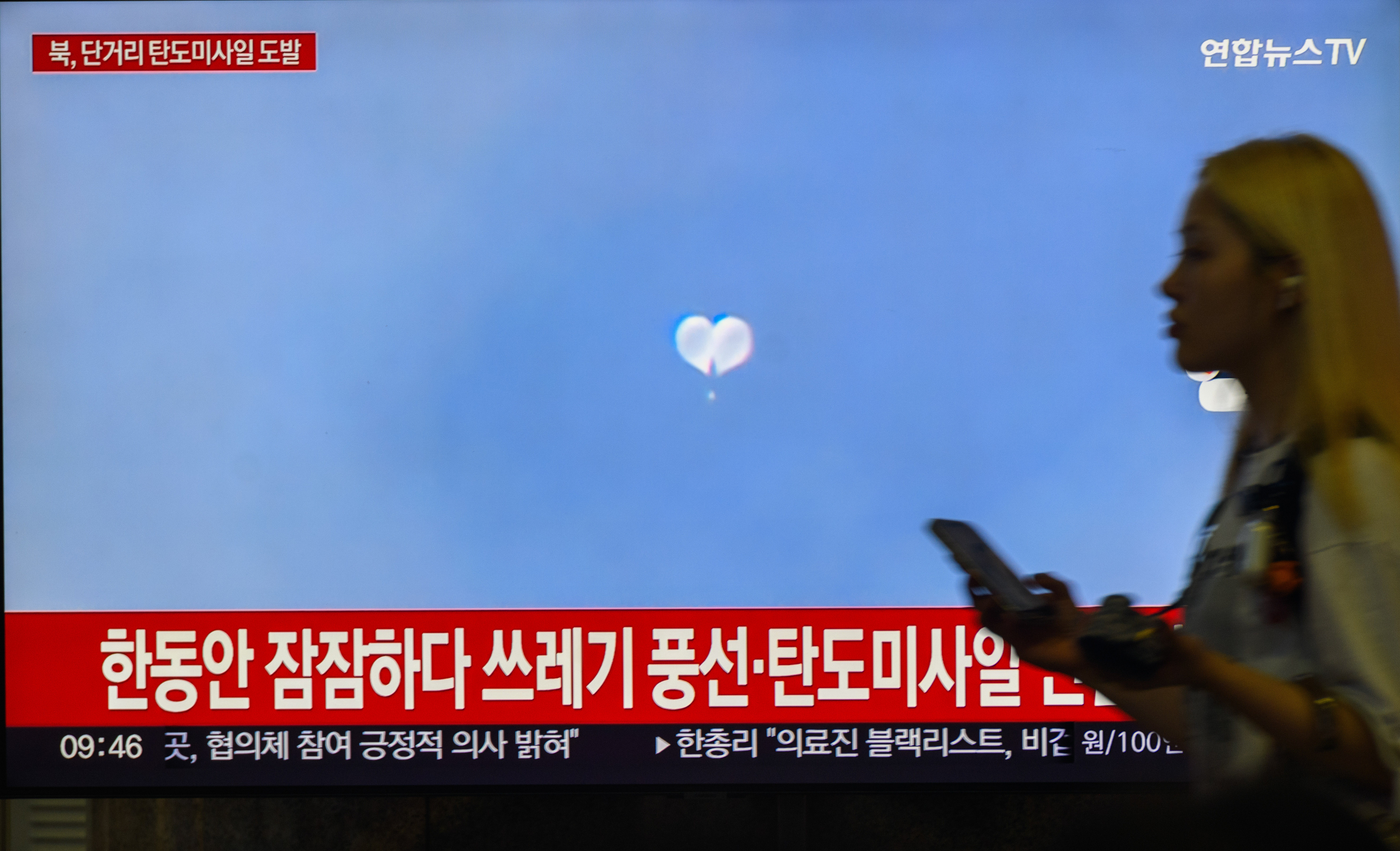 SEOUL, SOUTH KOREA - 2024/09/12: A woman was seen passing by the 24-hour Yonhap News TV broadcast at Yongsan Railway Station in Seoul, which displayed a news segment featuring a file image of North Korea's balloons. North Korea fired multiple short-range ballistic missiles toward the East Sea on September 12, the South Korean military said, a week after Pyongyang warned that South Korea and the United States would have to pay a "dear price" for their joint drills. (Photo by Kim Jae-Hwan/SOPA Images/LightRocket via Getty Images)