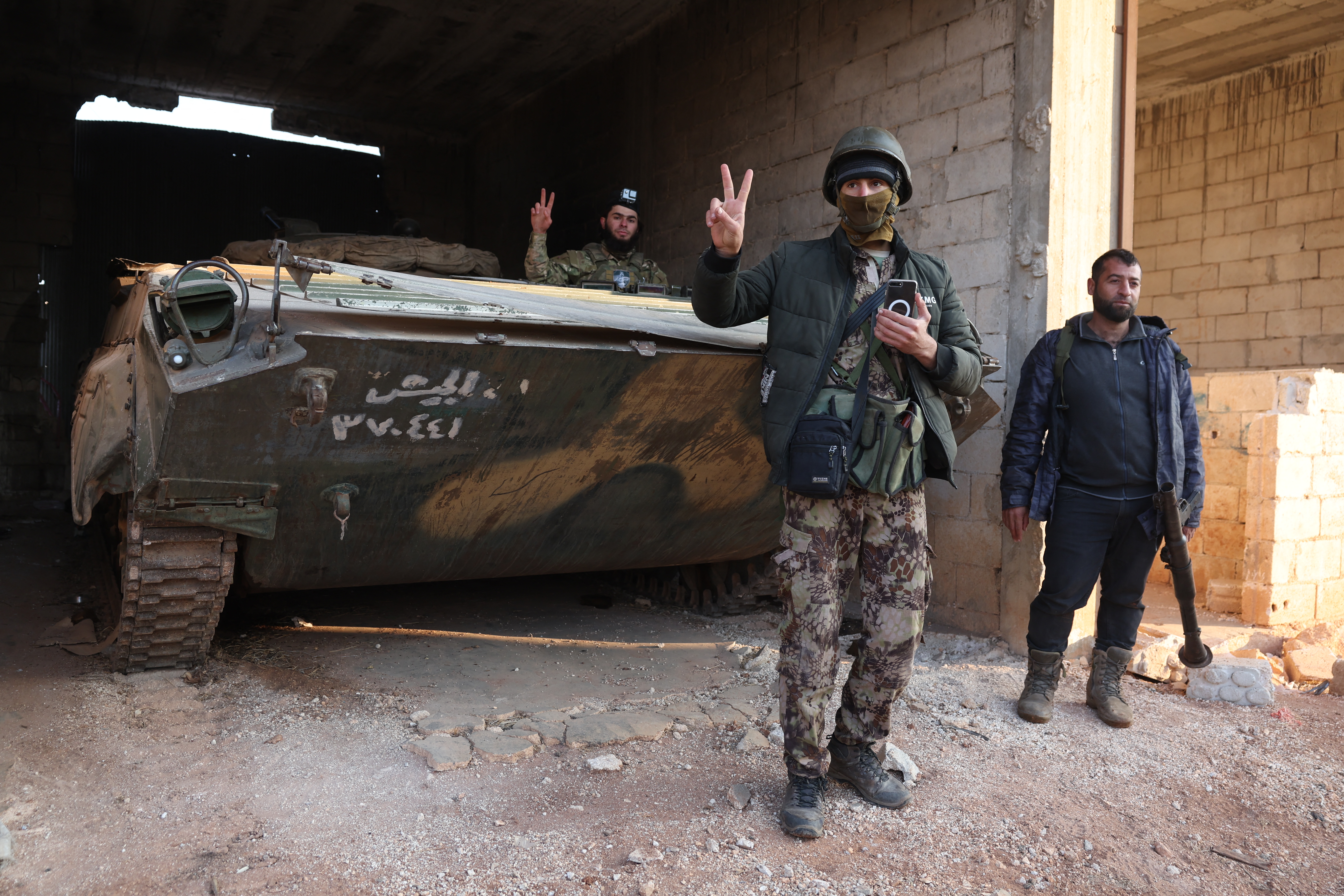 Rebel fighters pose in front of a seized Syrian Army tank in the village of Talhiyah, located east of the northwestern Syrian city of Idlib near the Taftanaz military airport, after the area was taken over by Jihadists and their Turkish-backed allies in the latest battles with government forces in the northern Syrian Aleppo province, on November 29, 2024. Hayat Tahrir al-Sham (HTS) jihadists and allied factions launched this week a shock offensive against Syrian government troops and sparked the deadliest battle the country has seen in years, with the violence killing so far 242 people, according to the Syrian Observatory for Human Rights. The war monitor said most of the victims were combatants on both sides but also including civilians. (Photo by Omar HAJ KADOUR / AFP) (Photo by OMAR HAJ KADOUR/AFP via Getty Images)